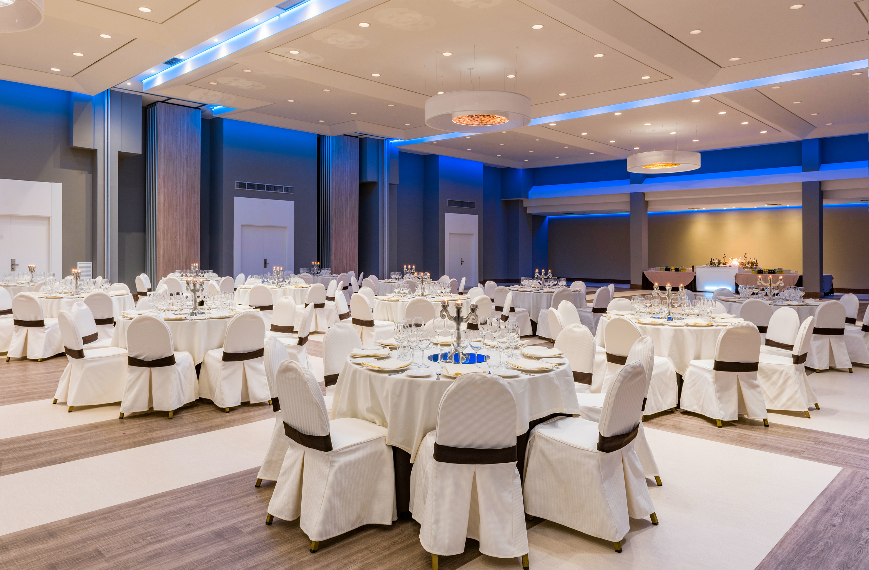 Elegant banquet hall set with white tables, chairs, and blue lighting.