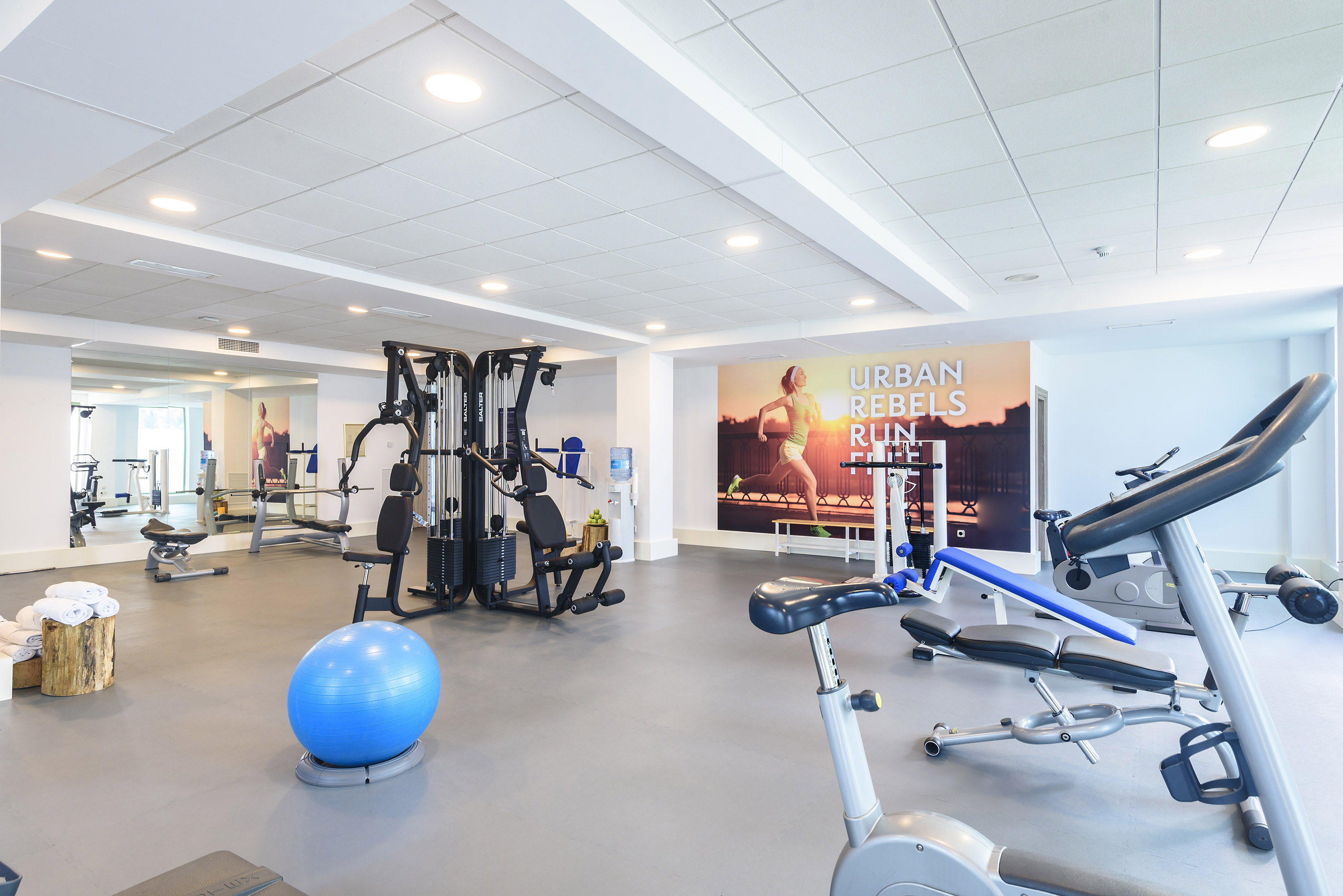 Well-equipped gym with fitness machines, stability ball, and running mural.