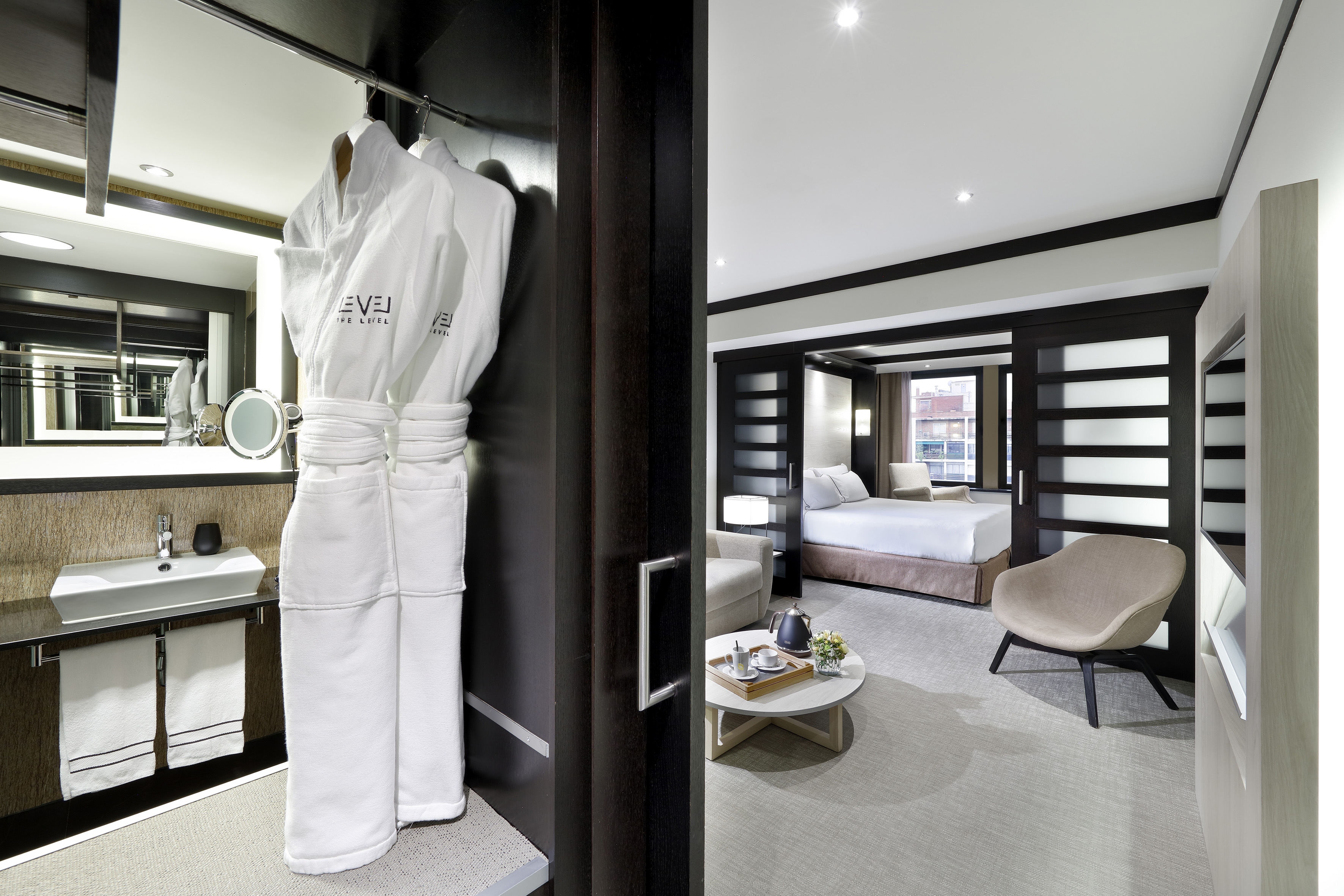 Luxury hotel suite with bathrobes, modern bedroom, and elegant vanity area.