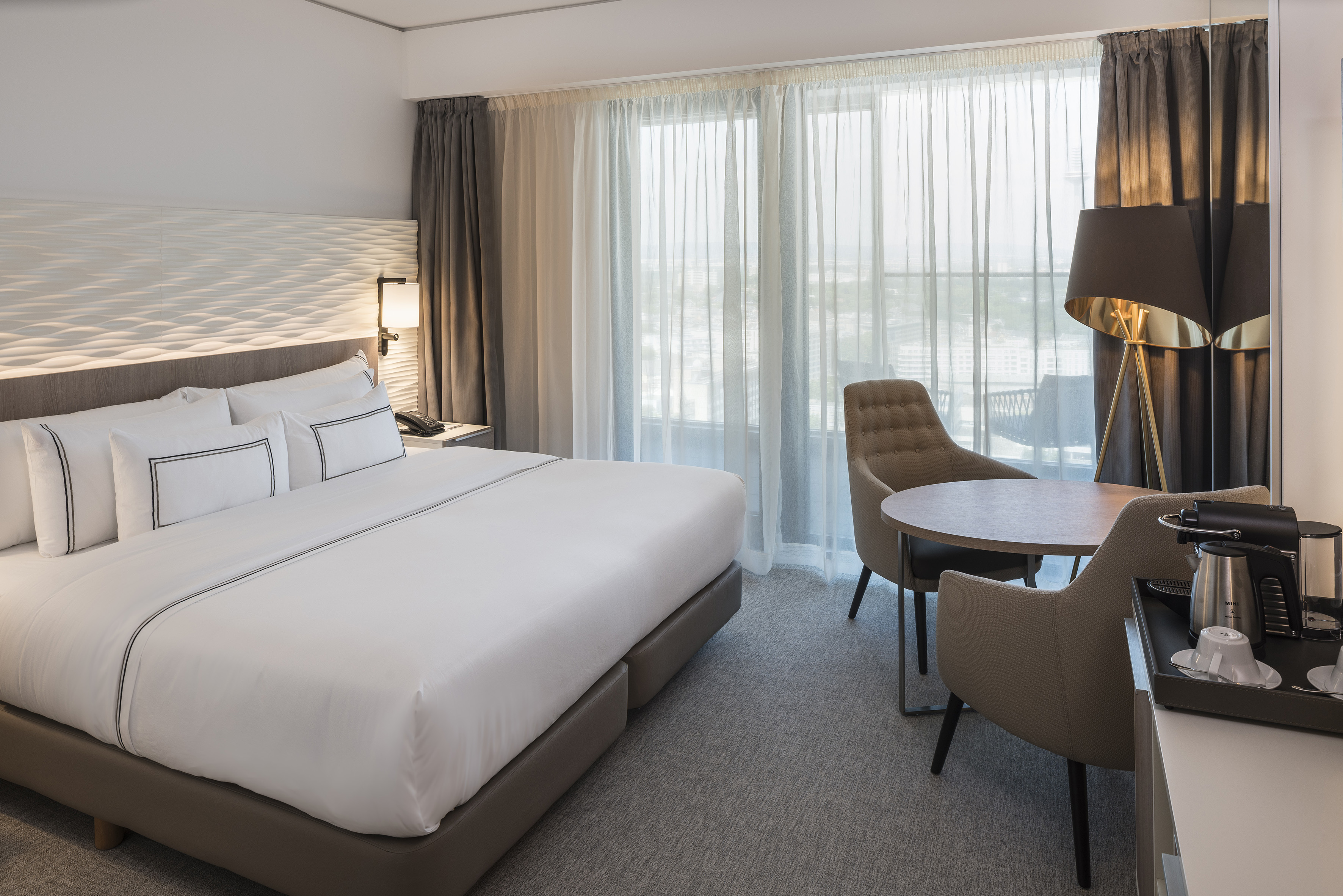 Modern hotel room with king bed, city view, and coffee station.