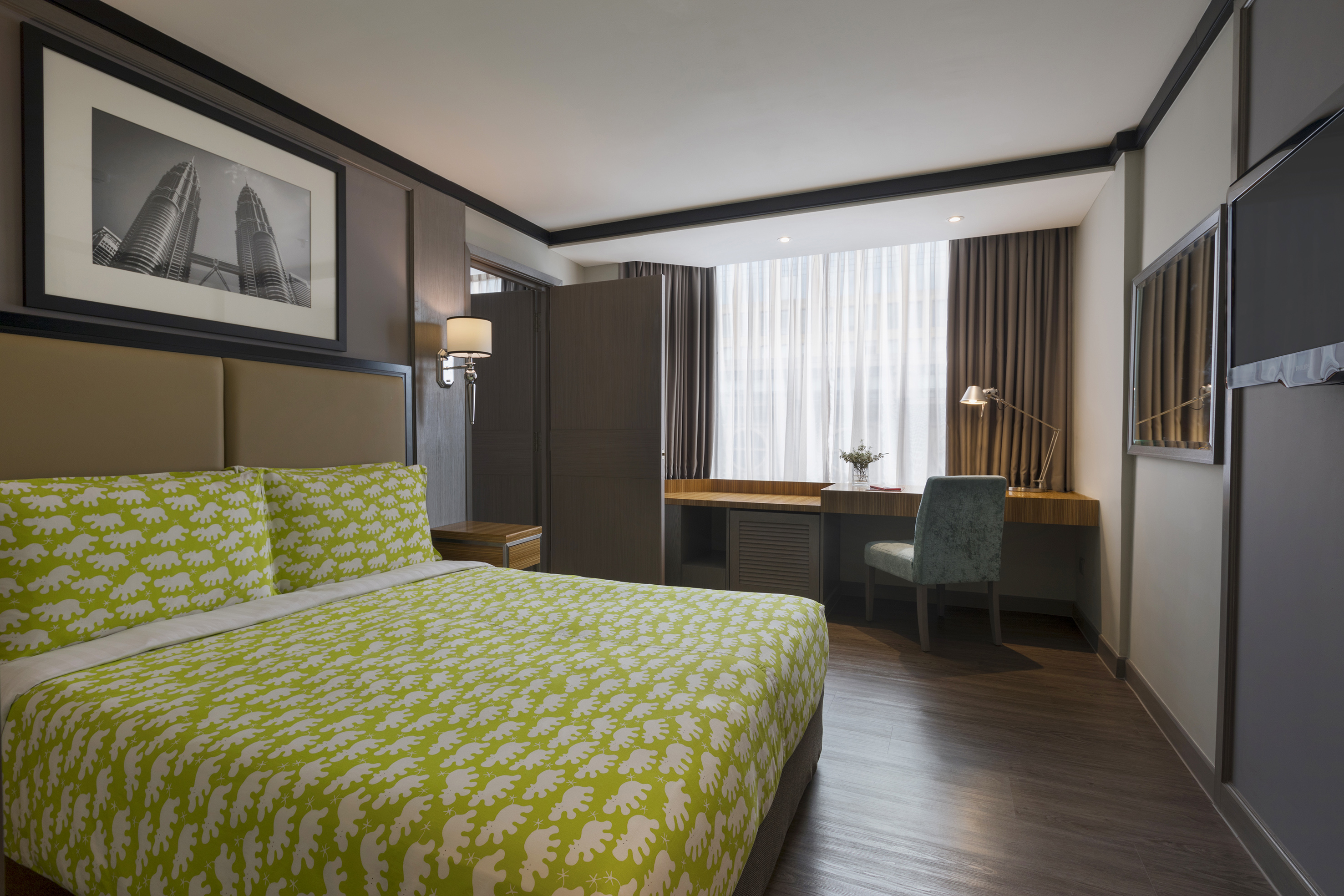 Modern hotel room with green patterned bed, desk, and Petronas Towers art.