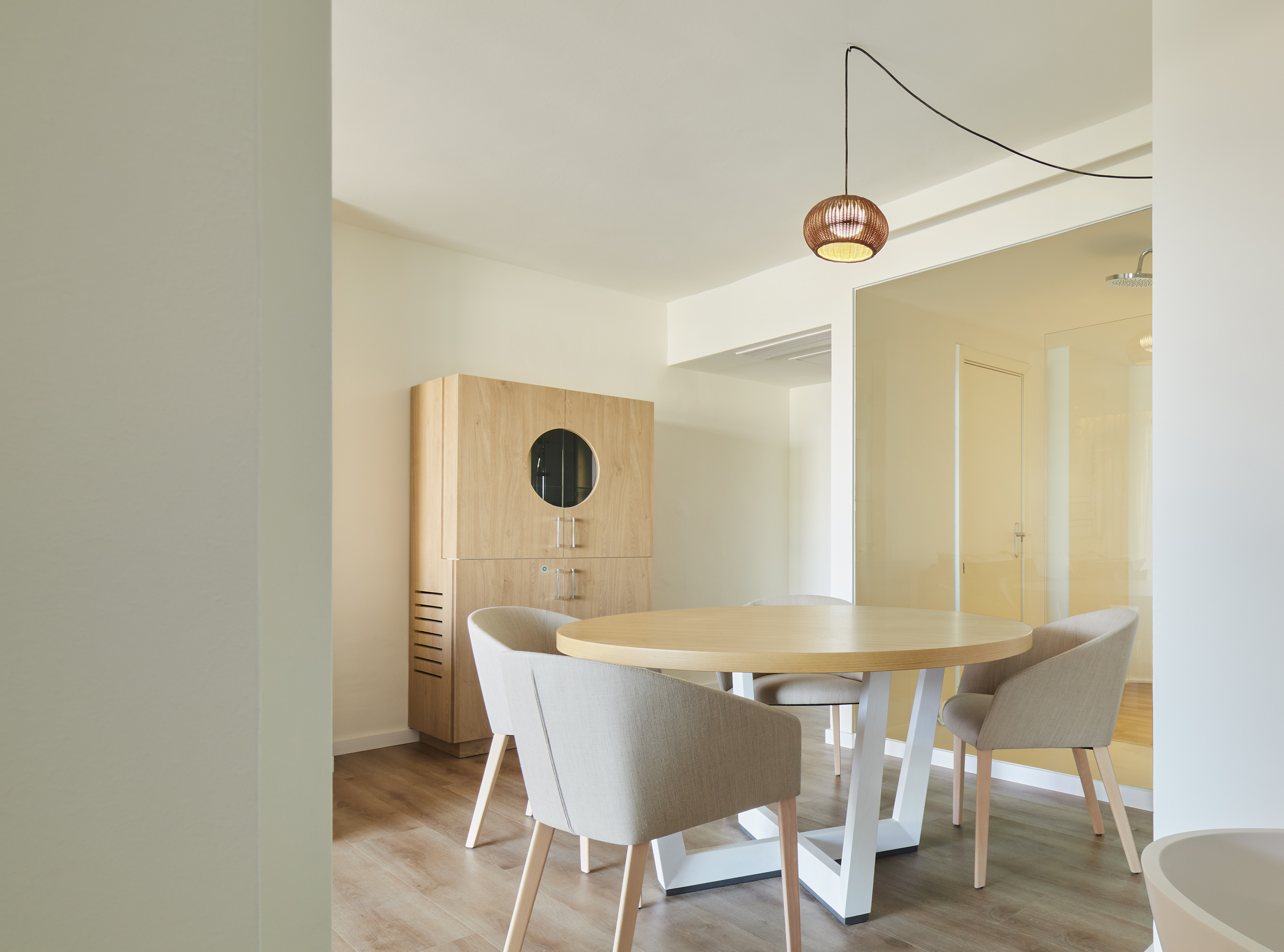 Modern dining area with round wooden table, upholstered chairs, and wood cabinet.