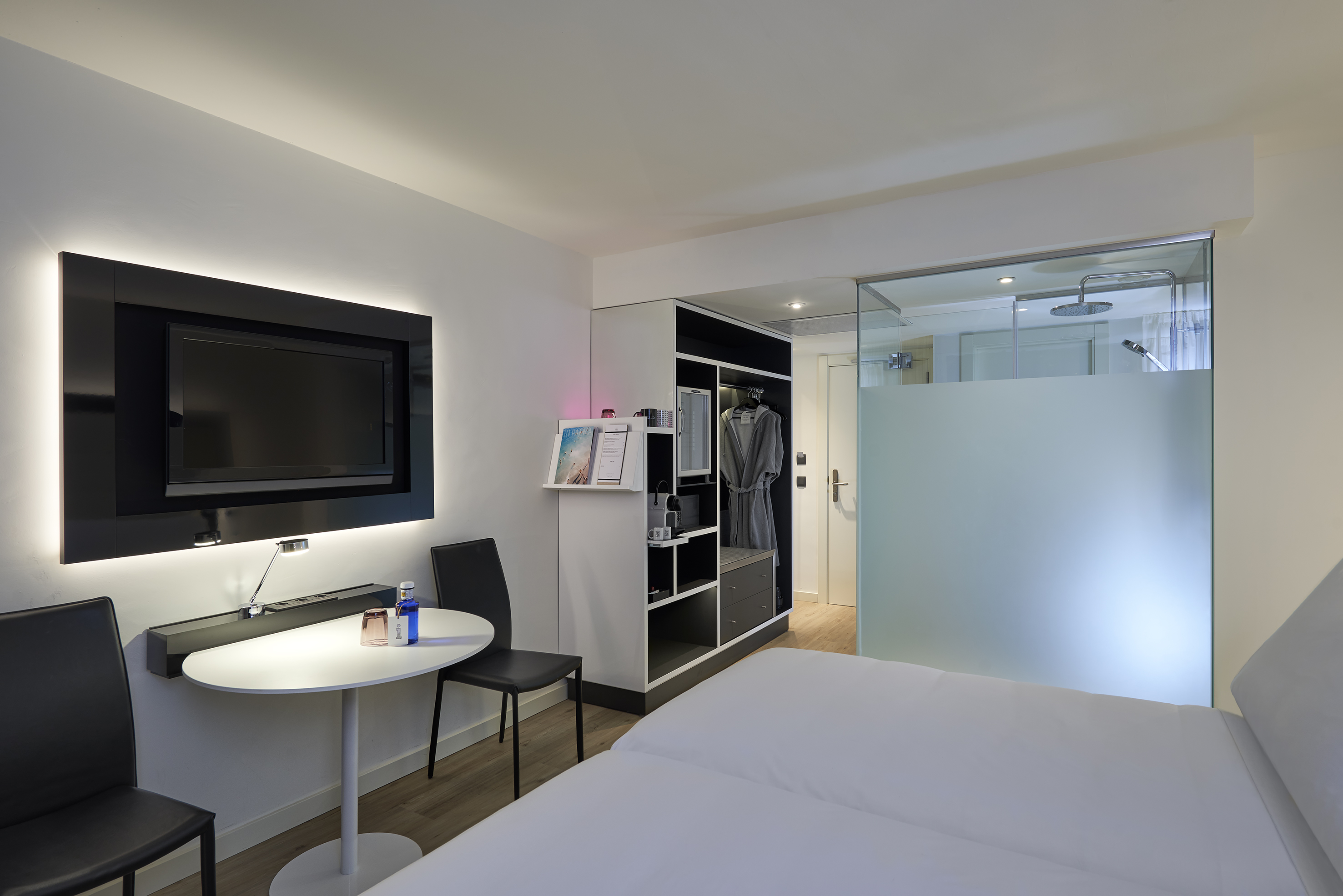 Modern hotel room with twin beds, wall TV, wardrobe, and glass shower.