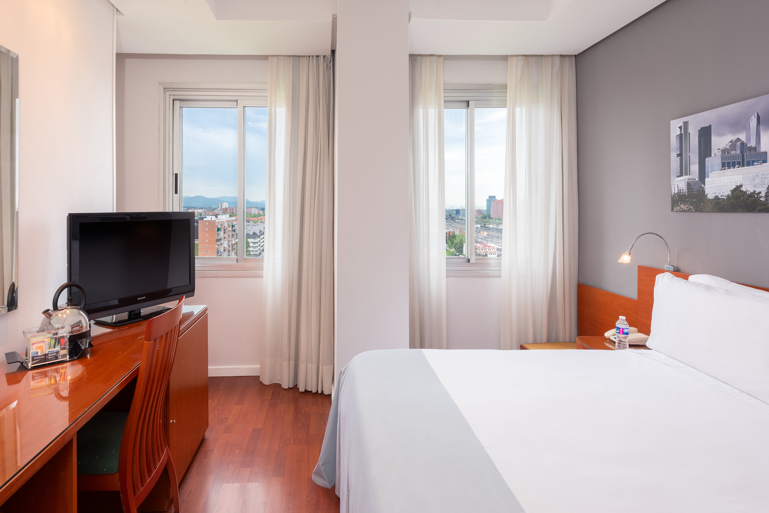 Modern hotel room with city view, comfortable bed, desk, and TV.