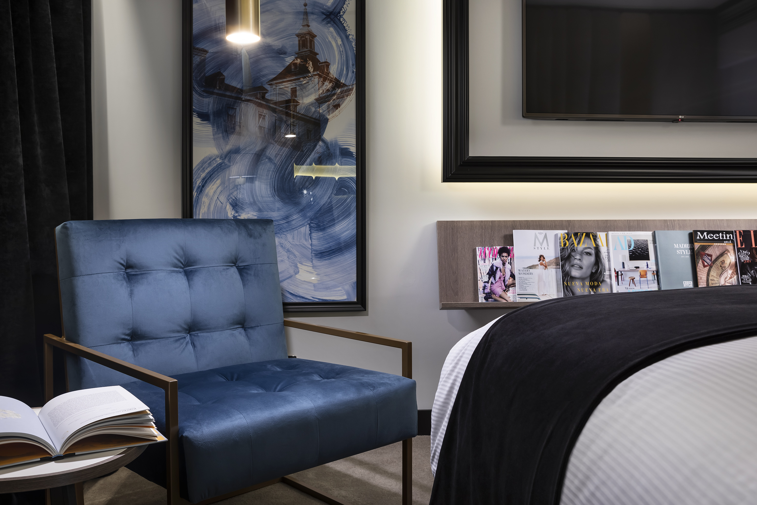 Blue velvet armchair in modern hotel room with abstract art and magazines.
