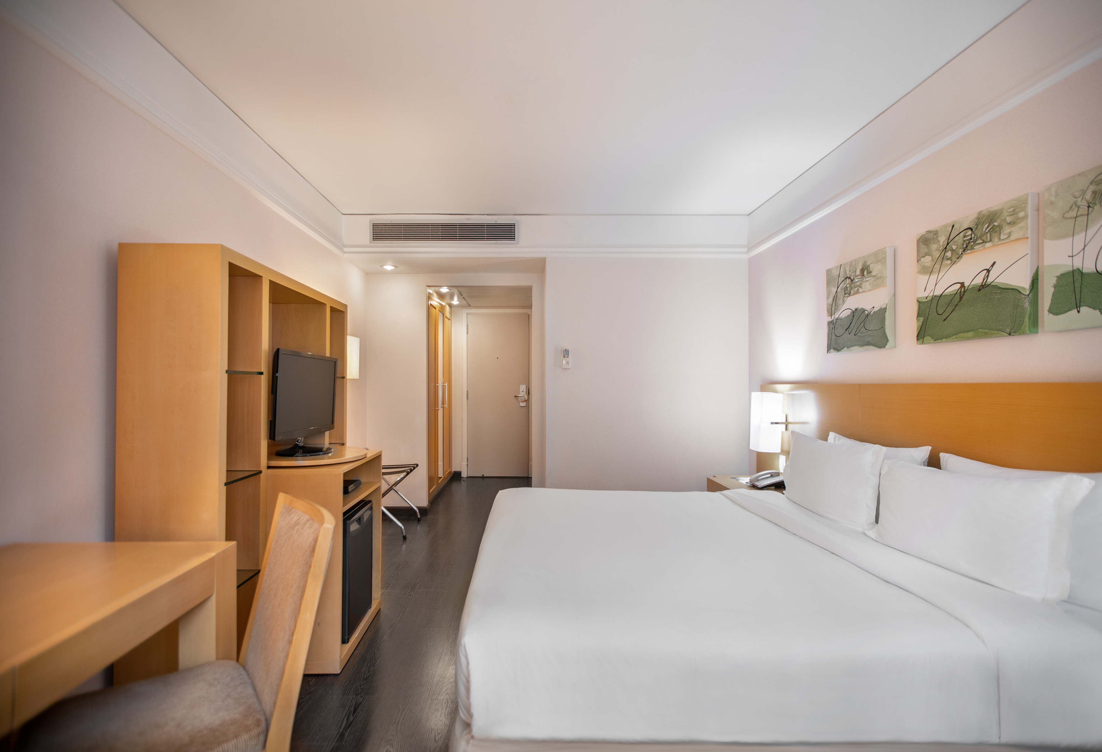 Modern hotel room with a large bed, desk, TV, and abstract wall art.