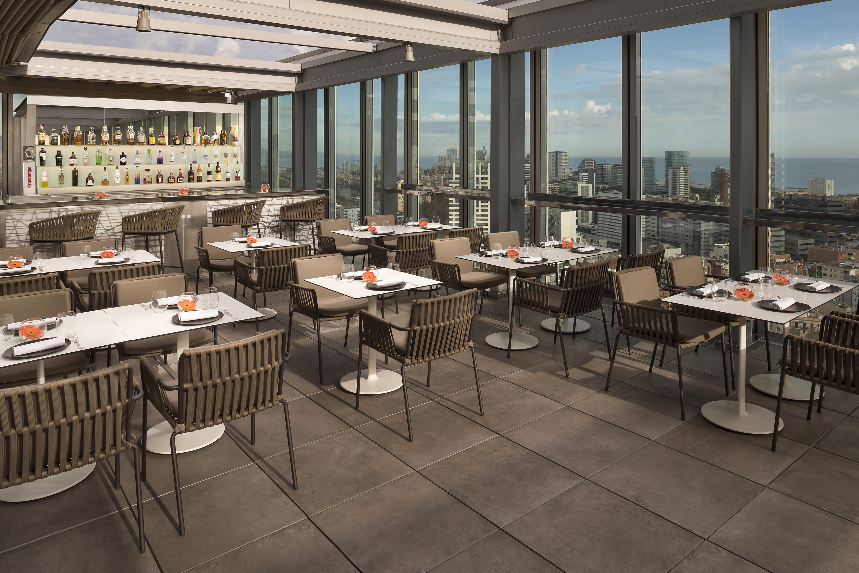 Modern rooftop bar and restaurant with city and ocean views, set tables.