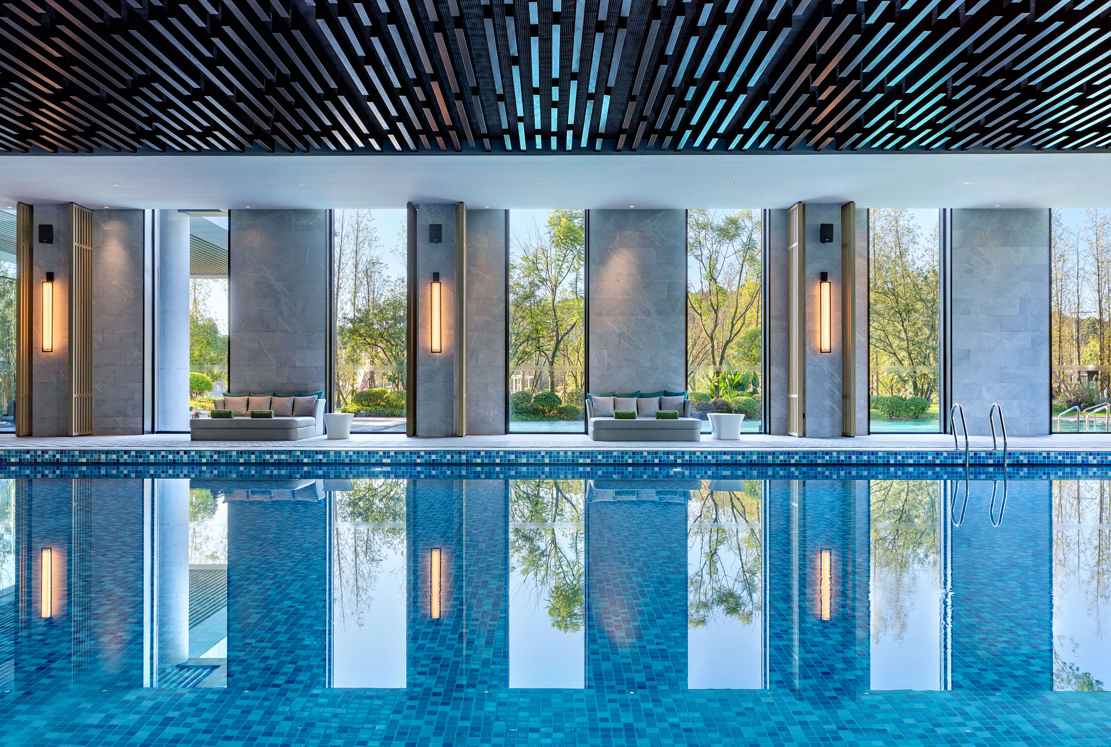 Modern indoor swimming pool with lush nature views and poolside lounge.