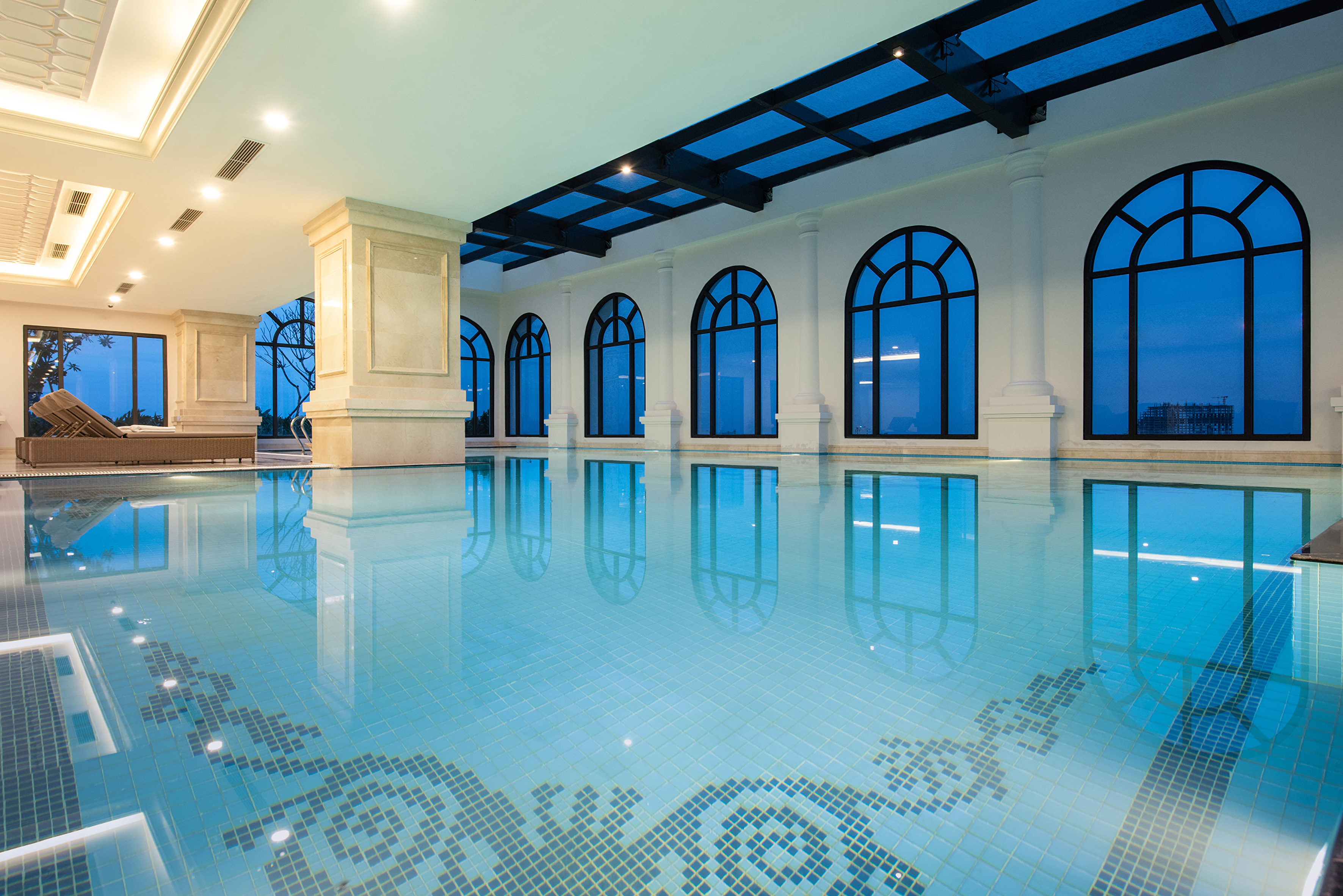 Luxurious indoor swimming pool with arched windows and light blue tiled water.