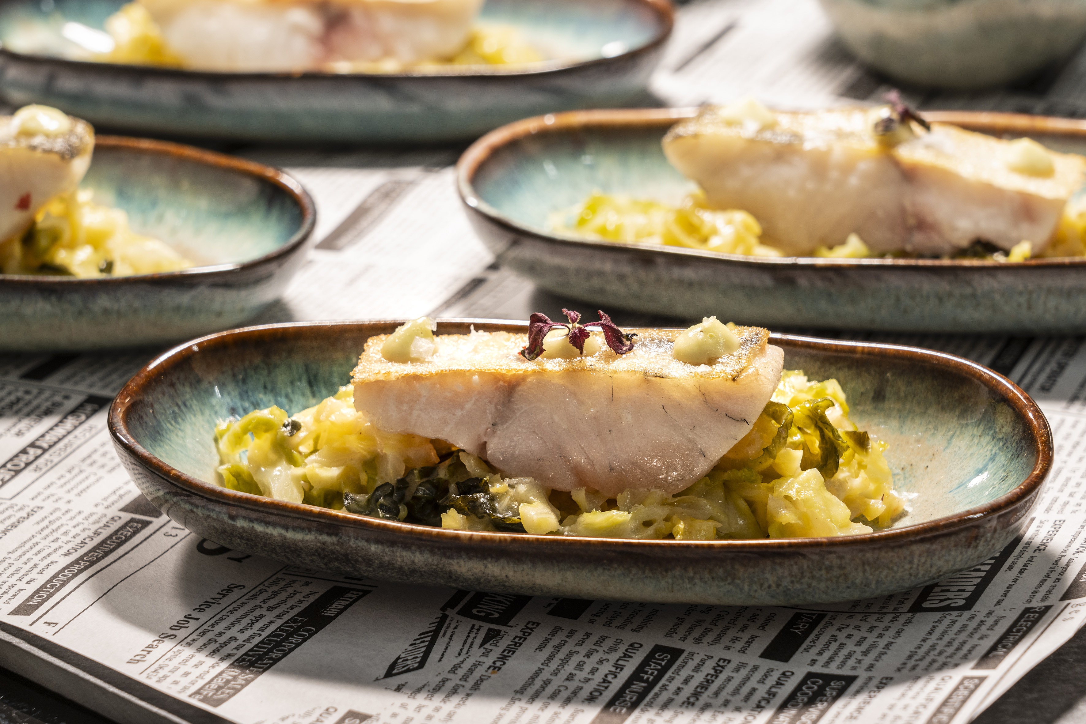 Pan-seared white fish on braised cabbage with a light sauce in ceramic dishes.