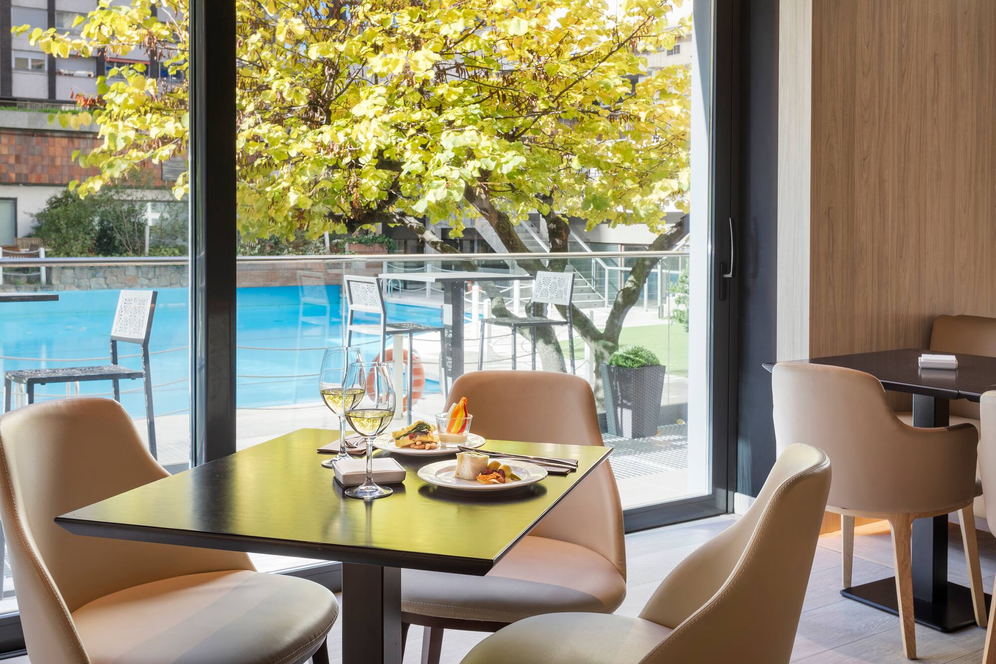 Restaurant dining table with wine, food, pool view, and autumn trees.