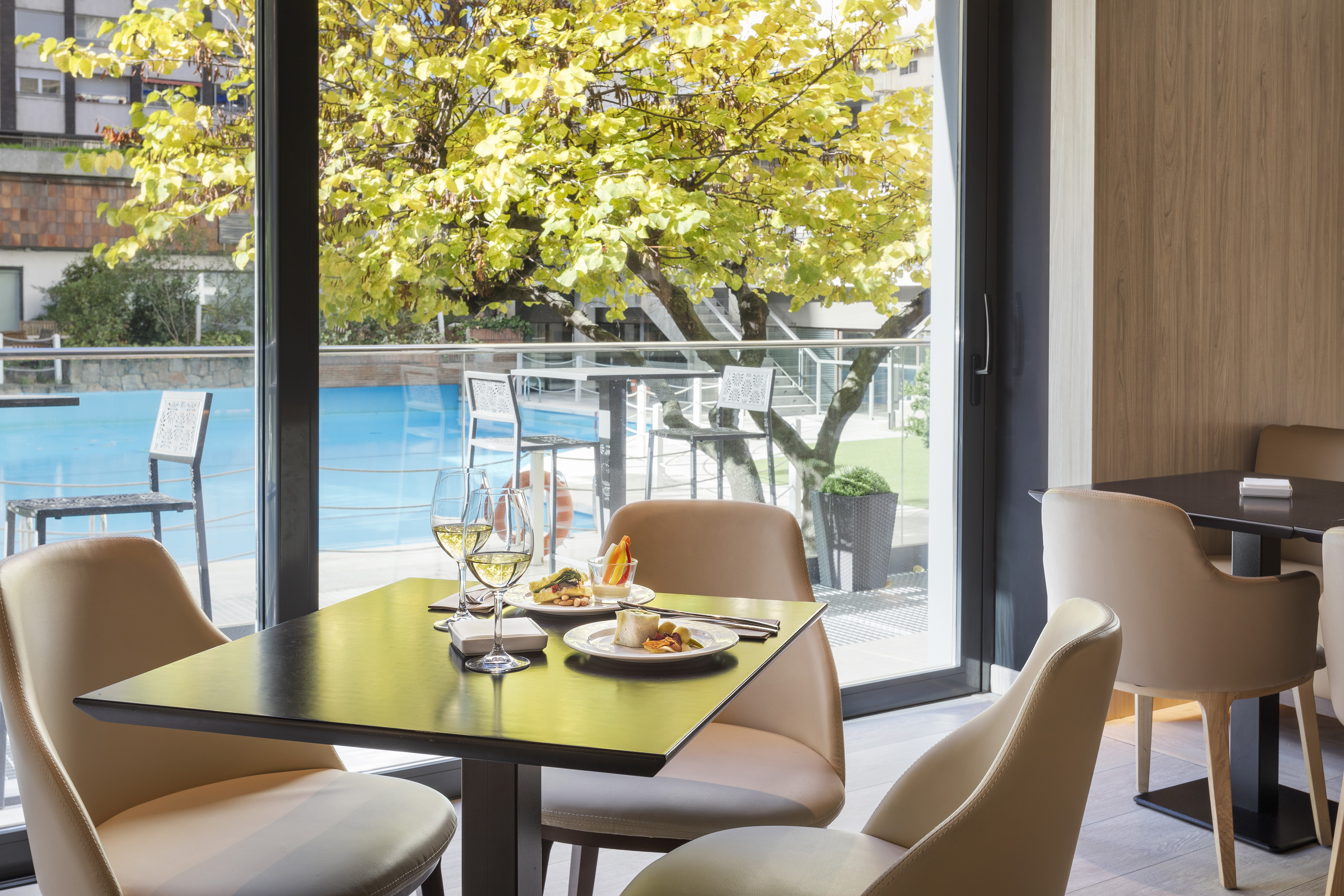 Restaurant dining table with wine, food, pool view, and autumn trees.
