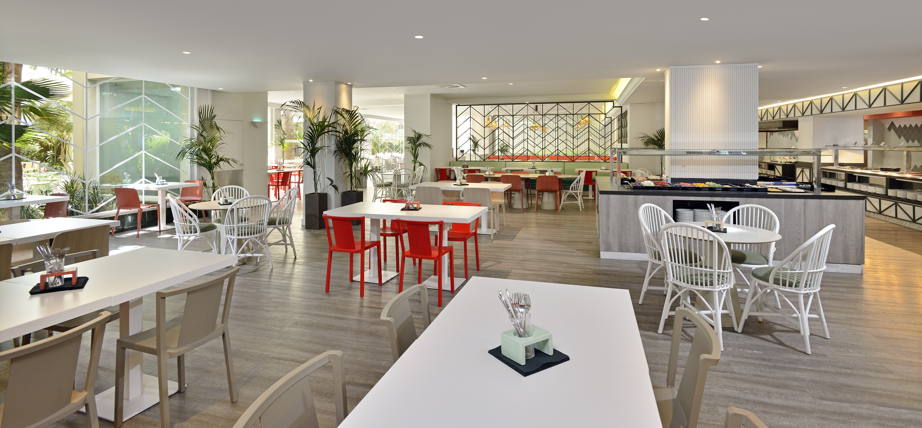 Modern restaurant interior with white tables, red chairs, and buffet area.