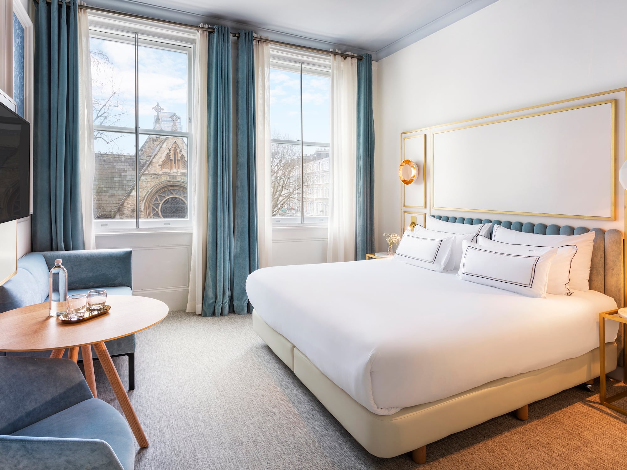 Elegant hotel bedroom with large bed, blue decor, and historic city view through windows.