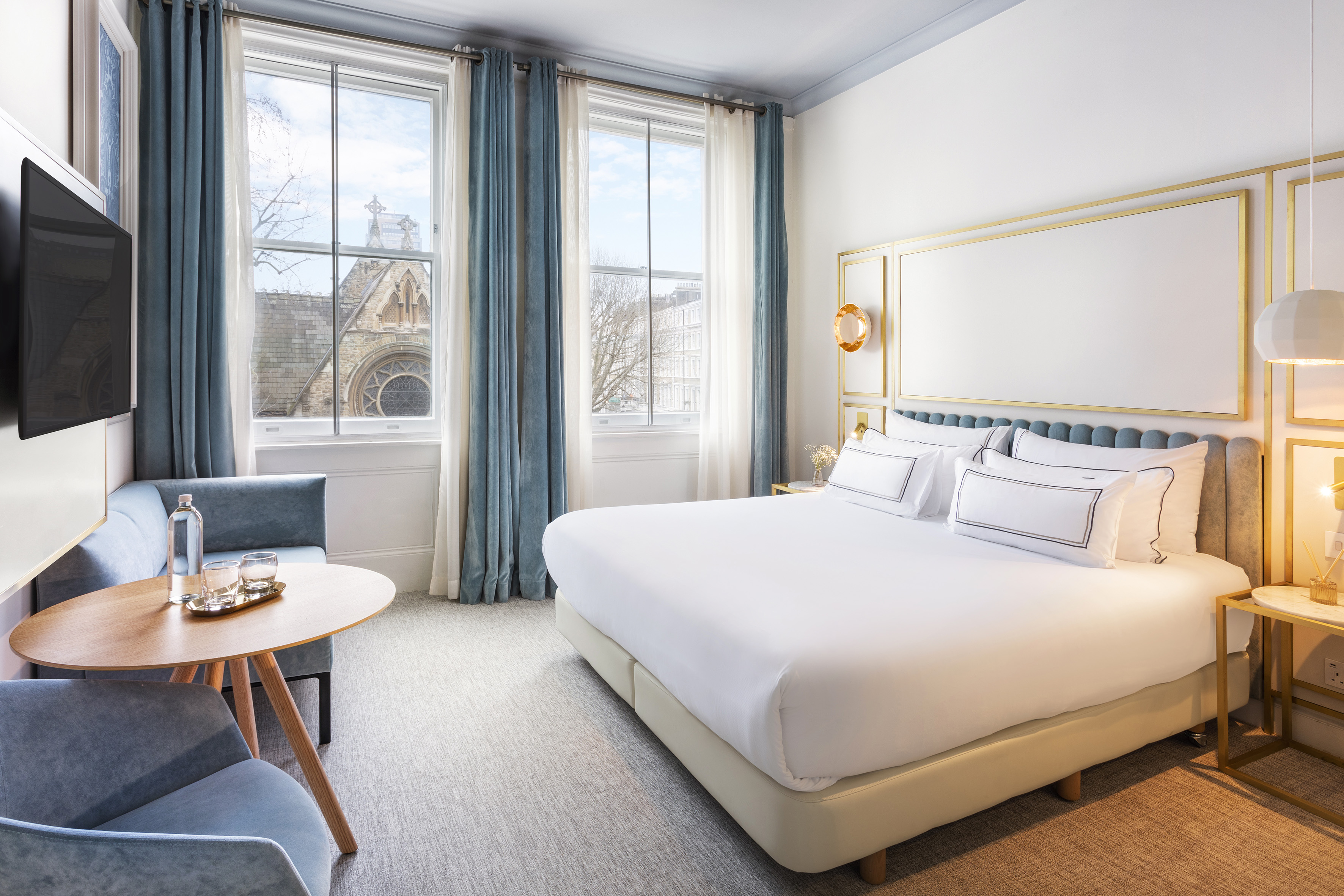 Elegant hotel bedroom with large bed, blue decor, and historic city view through windows.