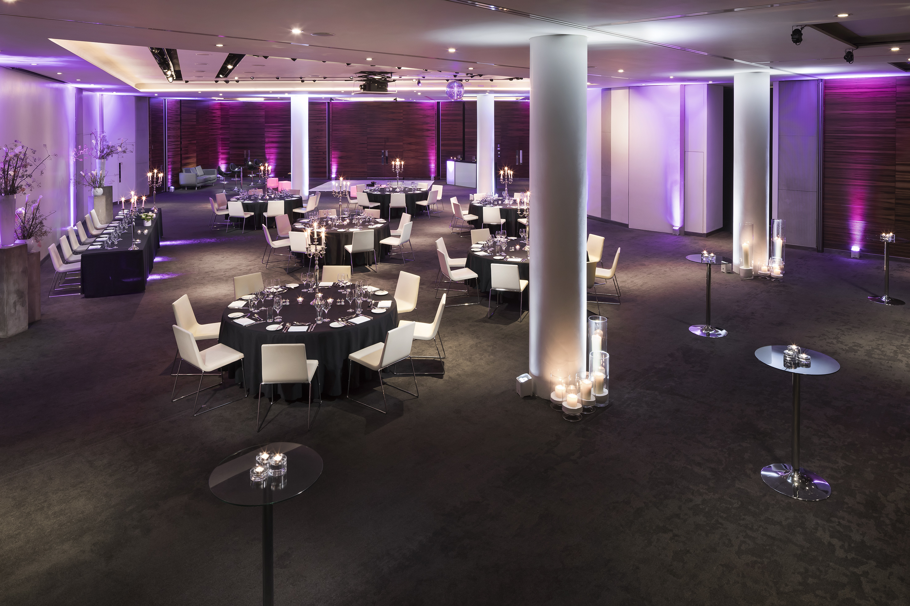 Modern event space with black tables, white chairs, and purple uplighting.
