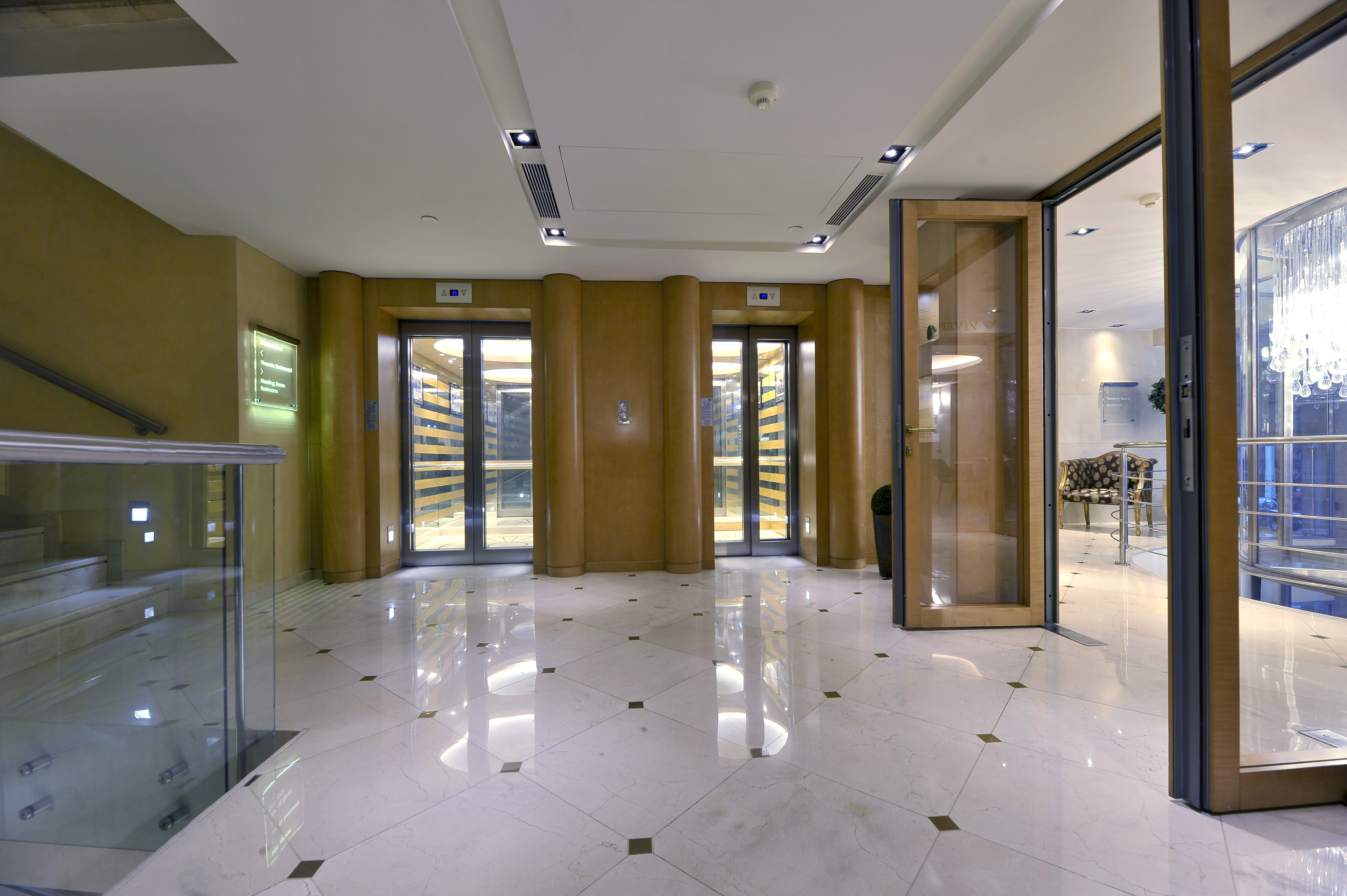 Modern luxury hotel lobby with two glass elevators and reflective marble floor.