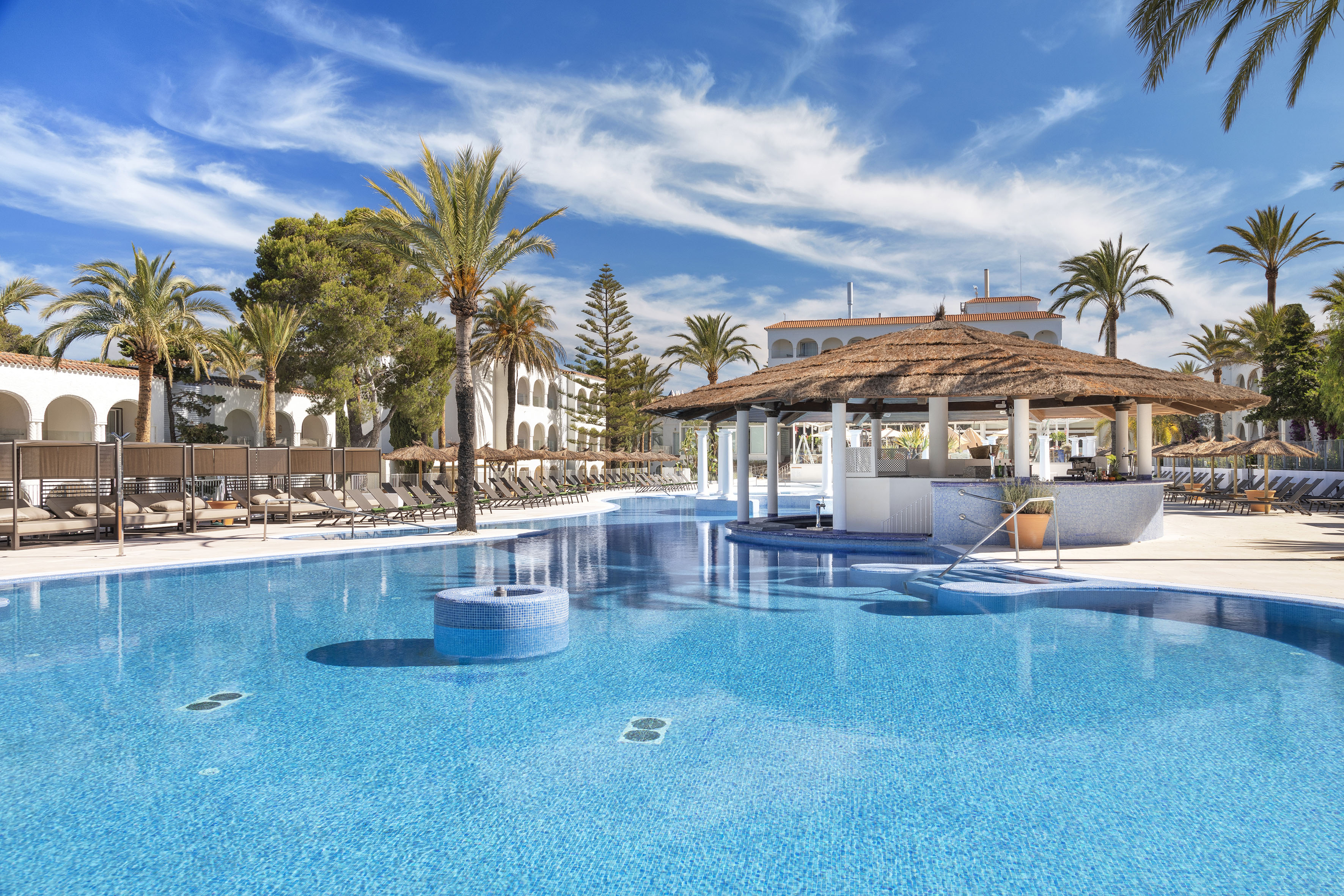 Tropical resort pool with swim-up bar, palm trees, and sun loungers.
