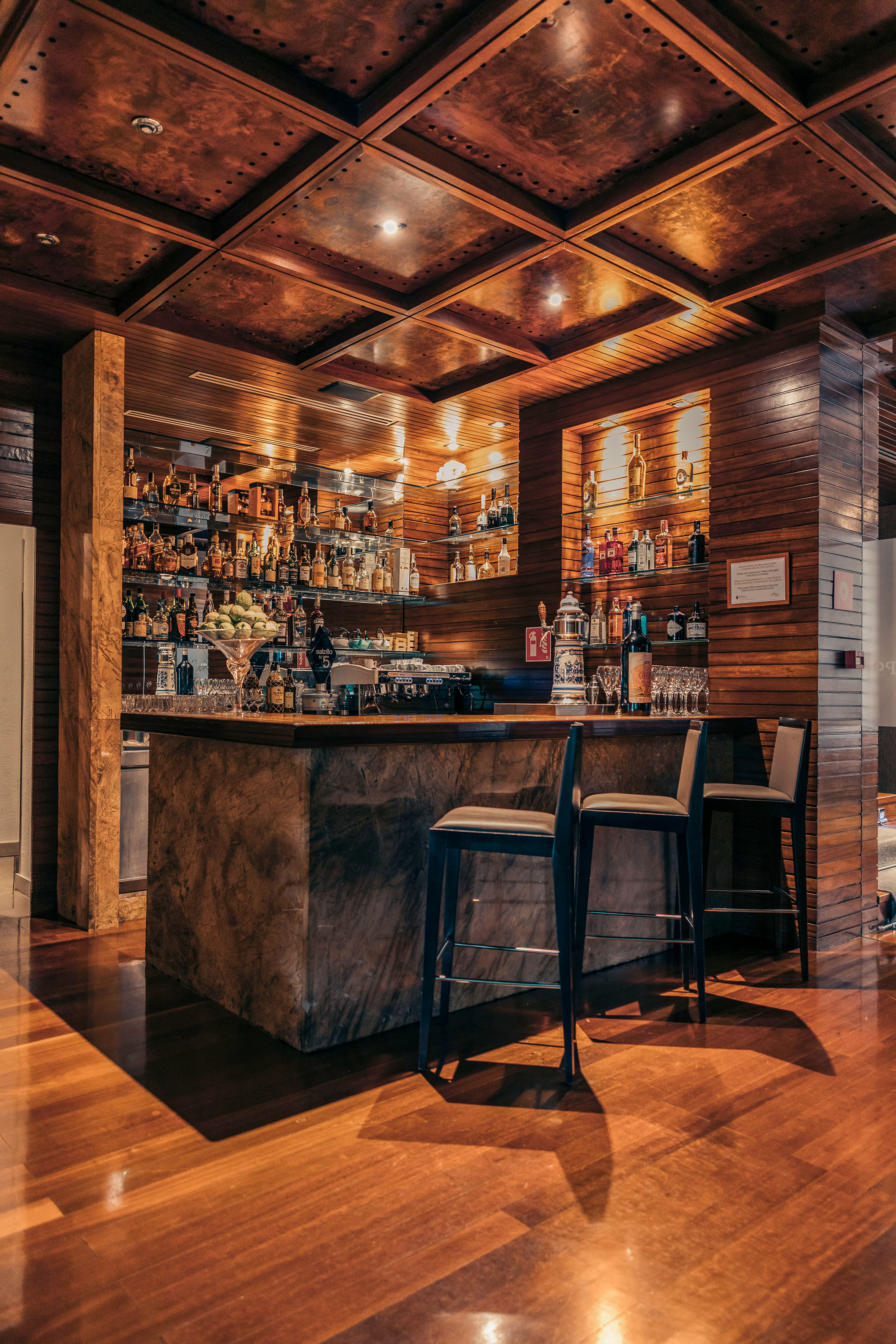 Elegant wood-paneled bar with full liquor display and bar stools.