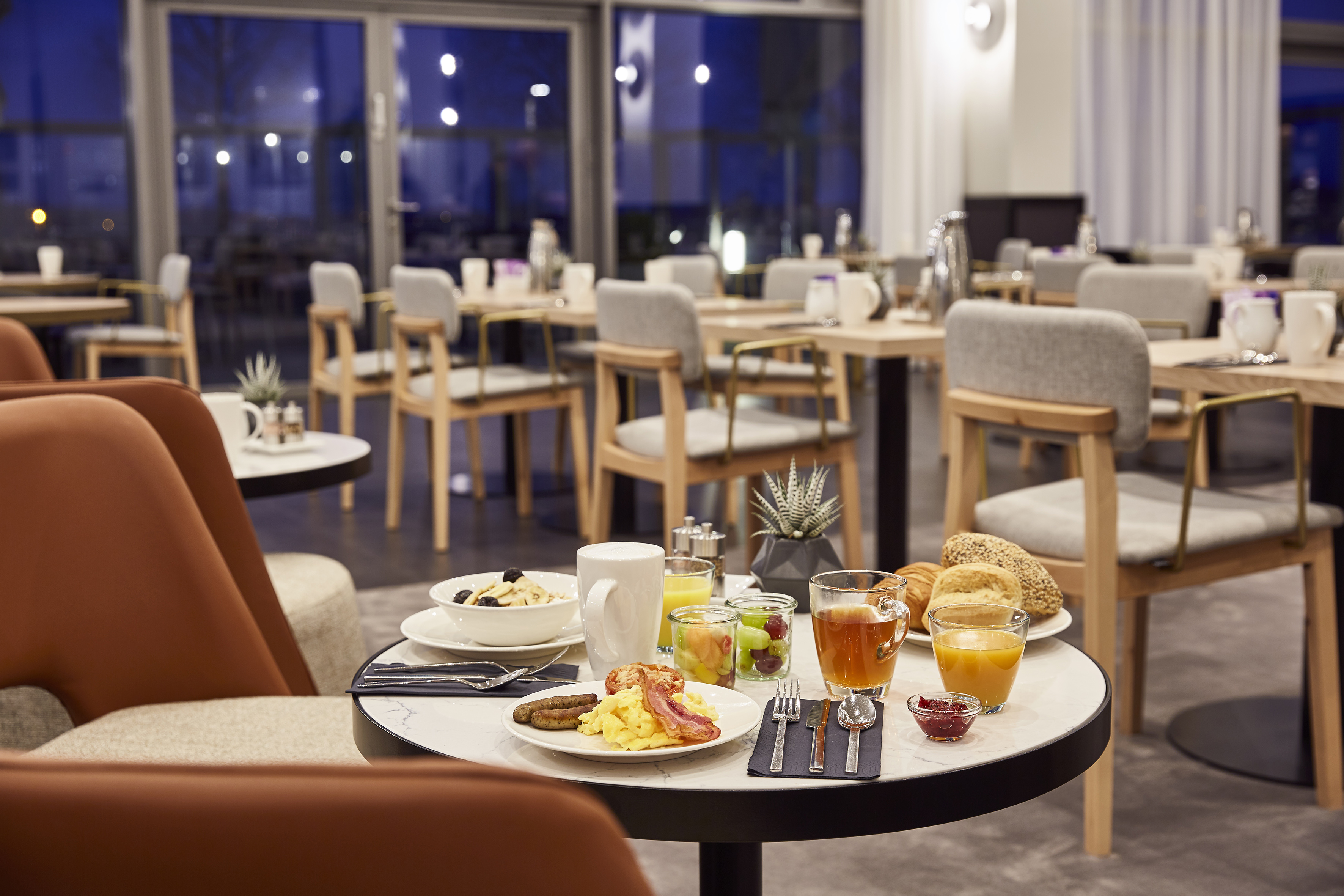 Hotel breakfast with eggs, bacon, and juice in a modern dining room.