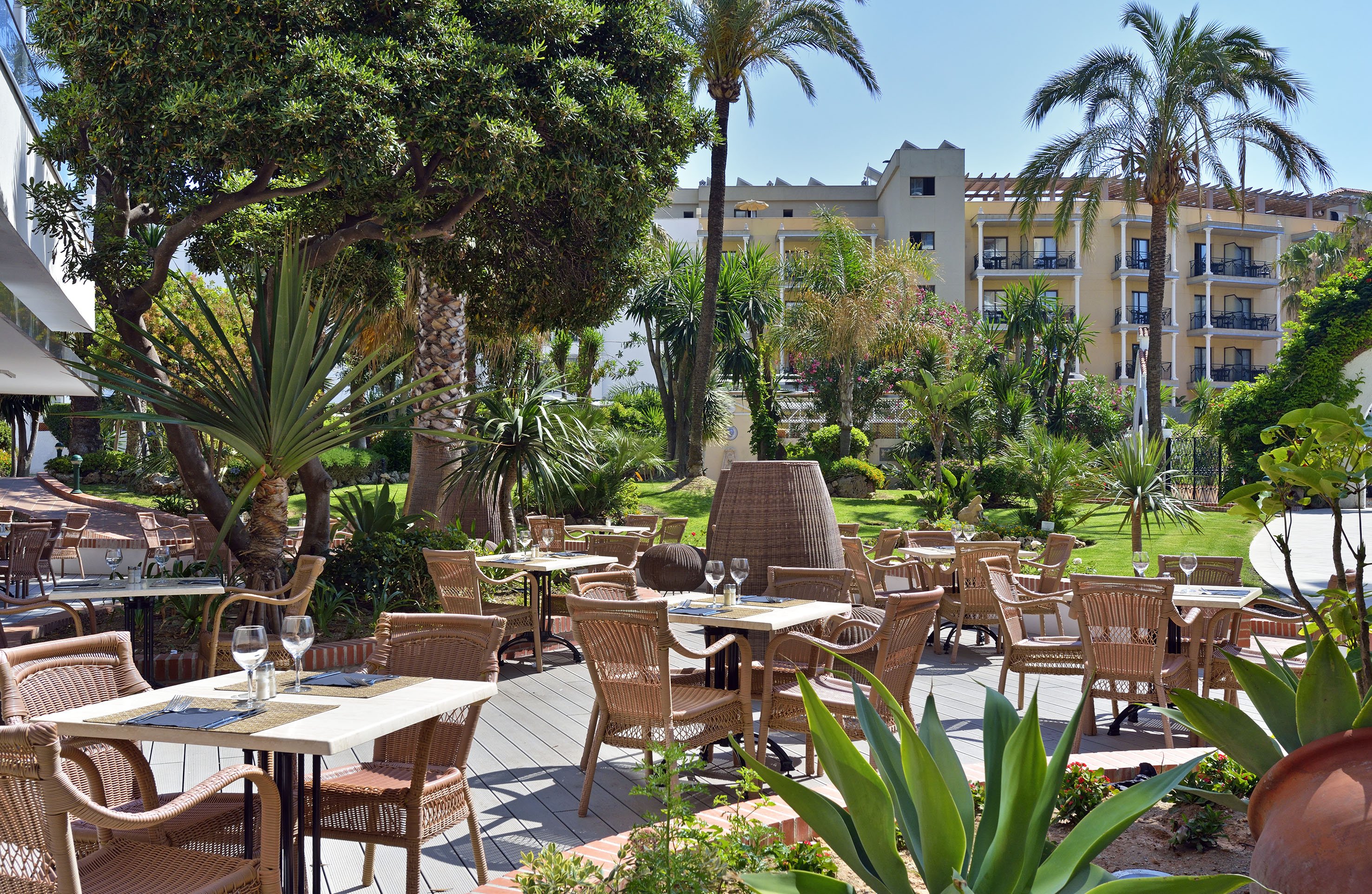 Outdoor dining terrace at a hotel with wicker tables and tropical garden.