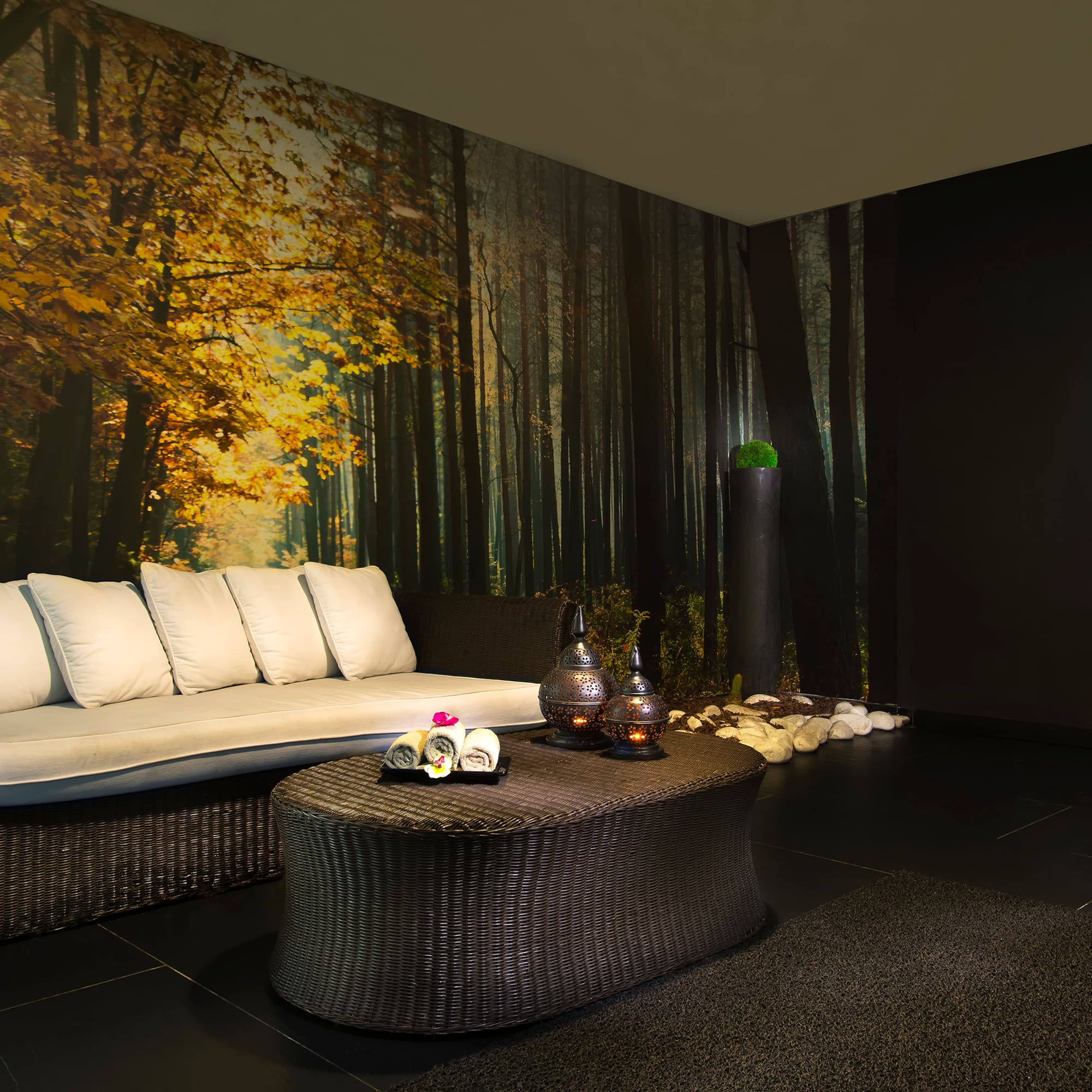 Spa lounge with autumn forest mural, wicker sofa, and decorative lanterns.