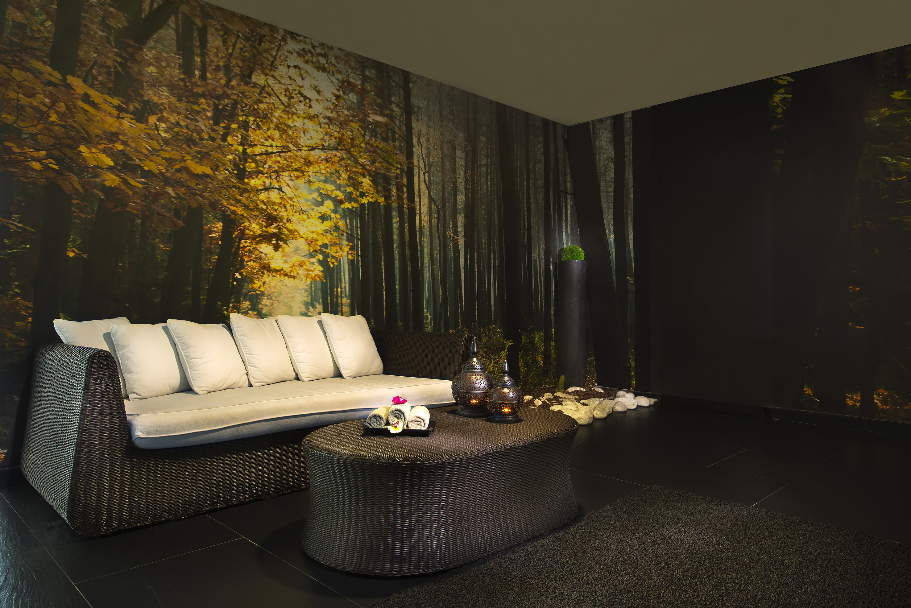 Spa lounge with wicker sofa, forest wall mural, and glowing lanterns.