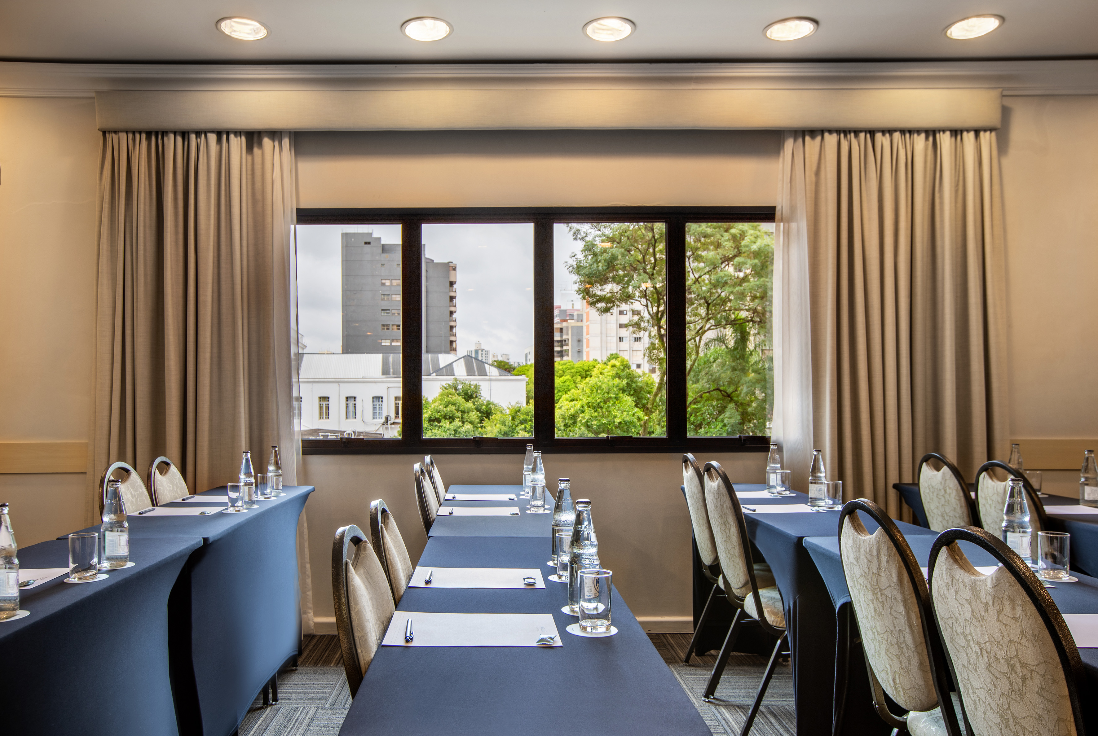 Professional meeting room with blue tables, chairs, water, cityscape.