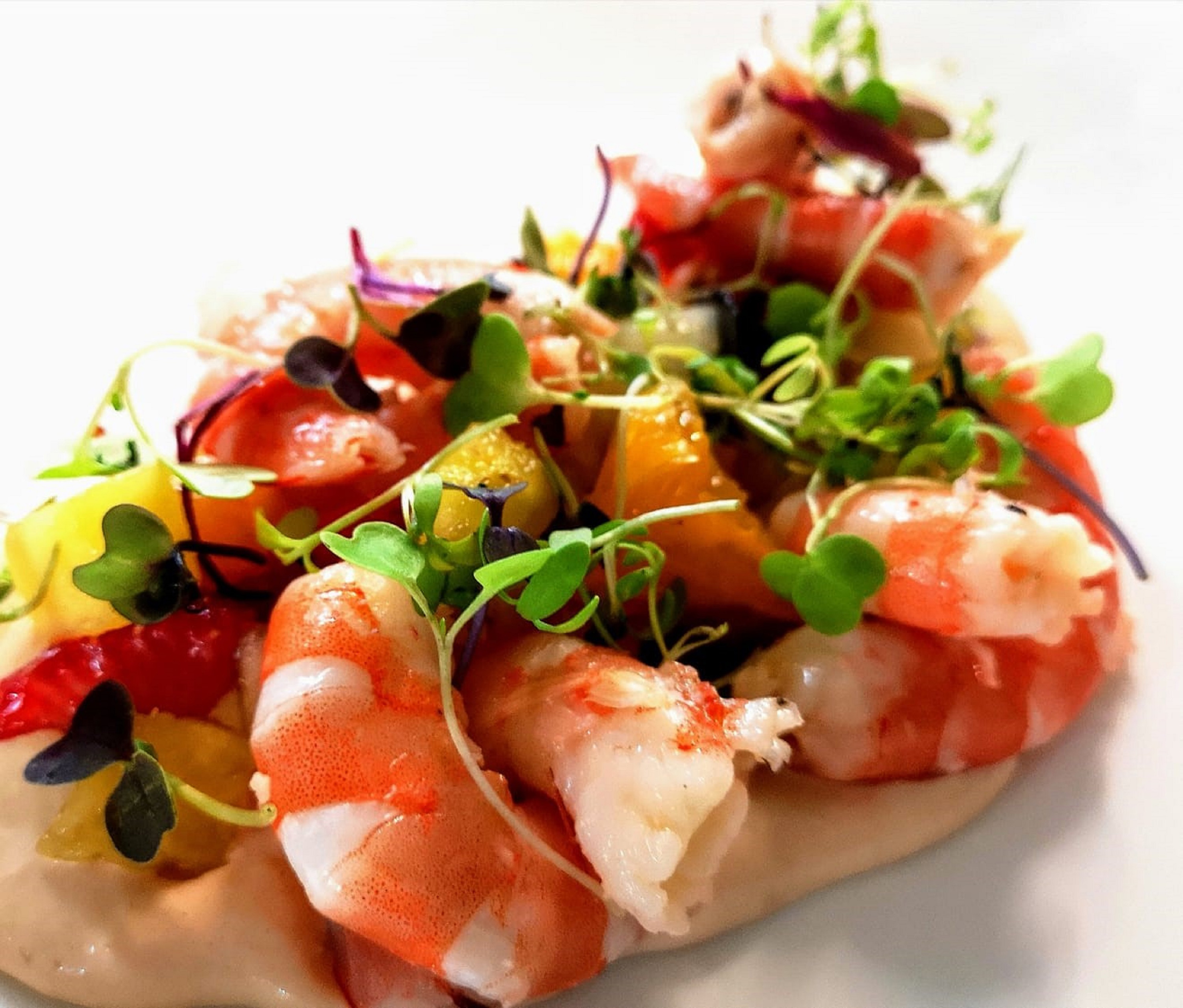 Gourmet shrimp appetizer with colorful fruit, microgreens, and creamy sauce.