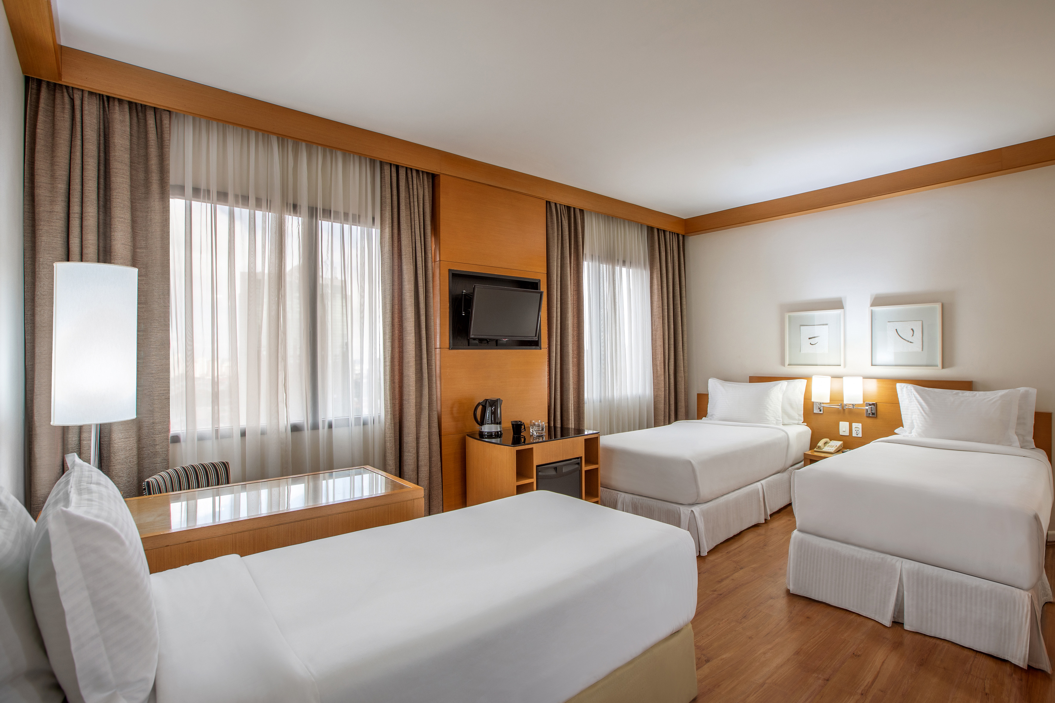 Comfortable hotel triple room with three twin beds, TV, and wooden floor.