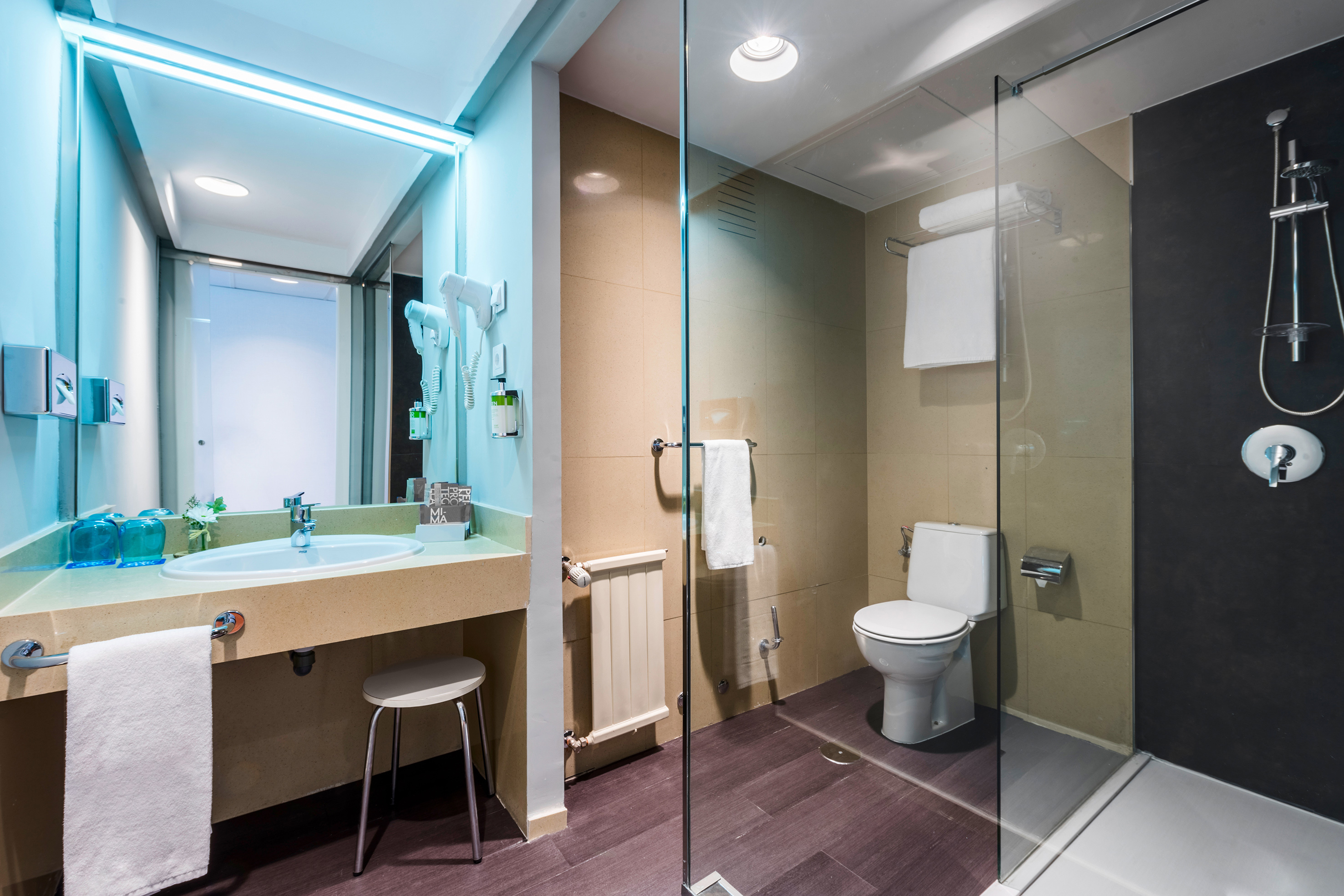 Modern hotel bathroom with vanity, lit mirror, toilet, and glass shower.
