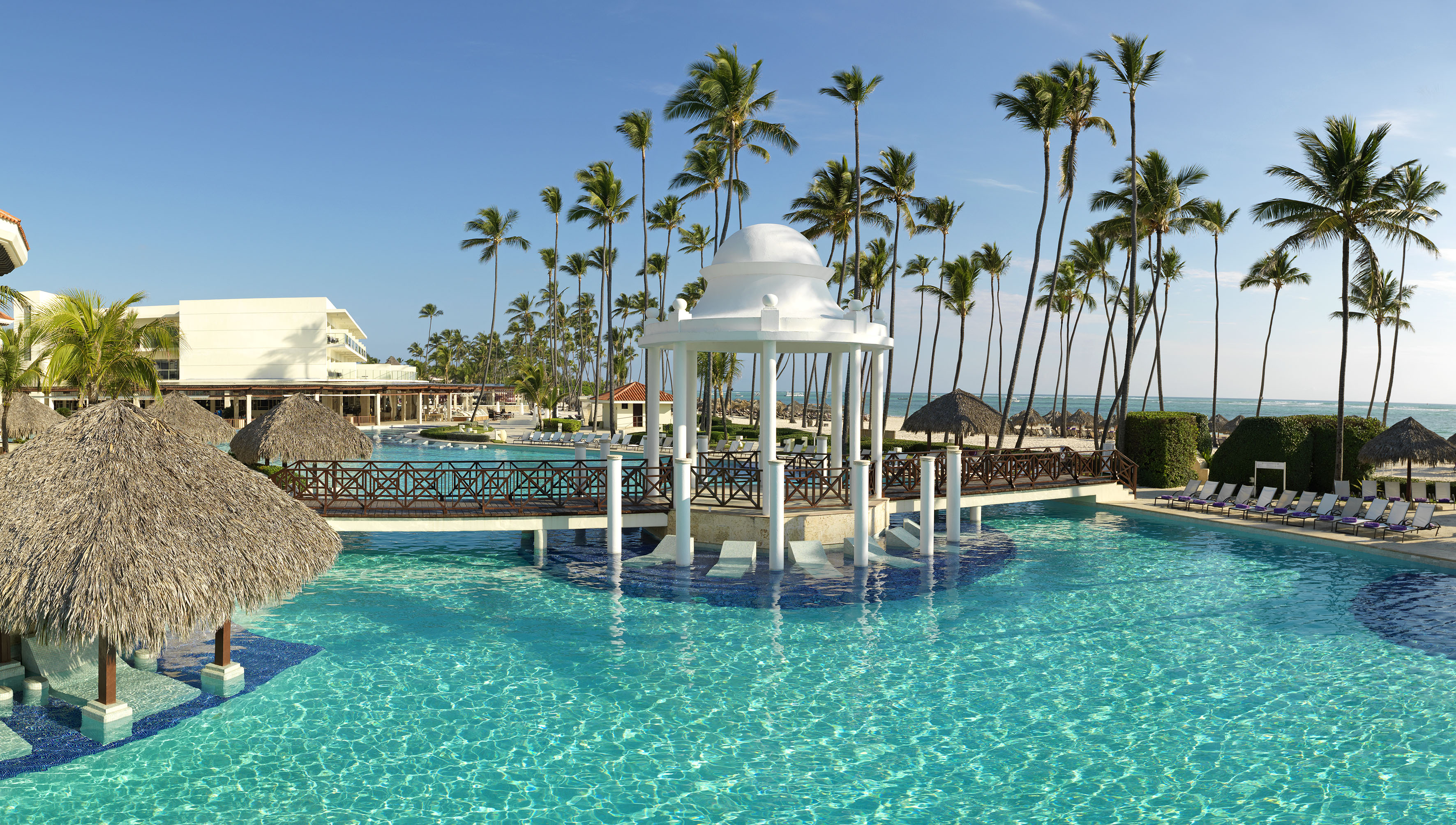 Tropical resort pool with white gazebo, palm trees, and beach in background