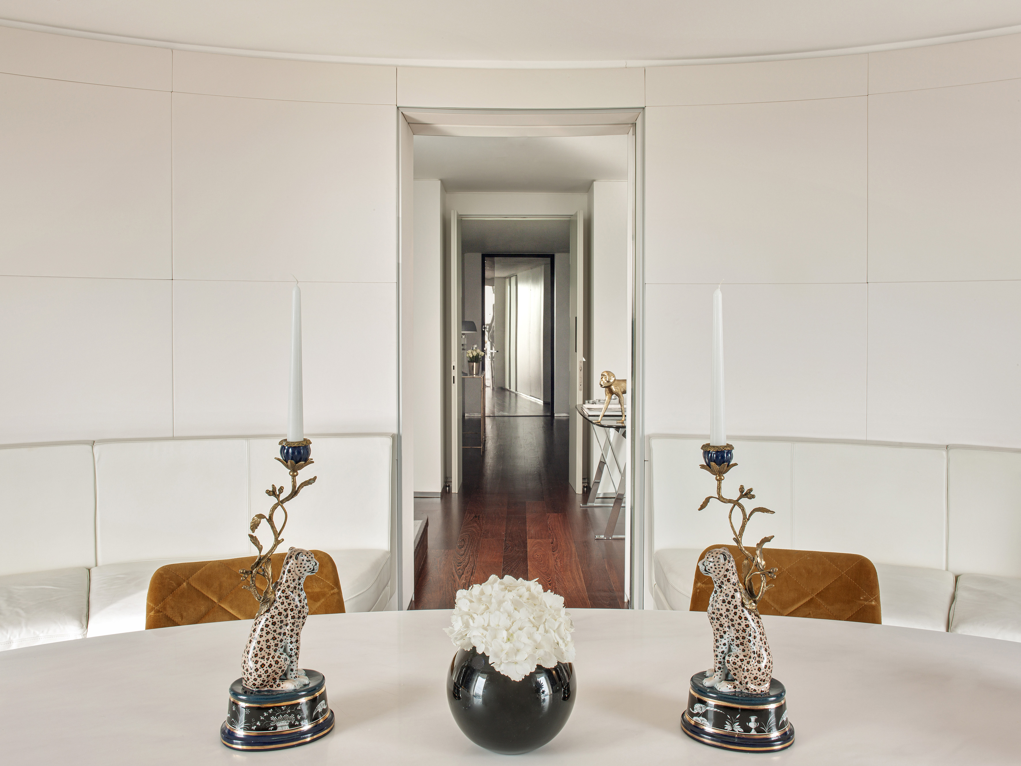 White dining room table, leopard candelabras, flowers, and hallway beyond.