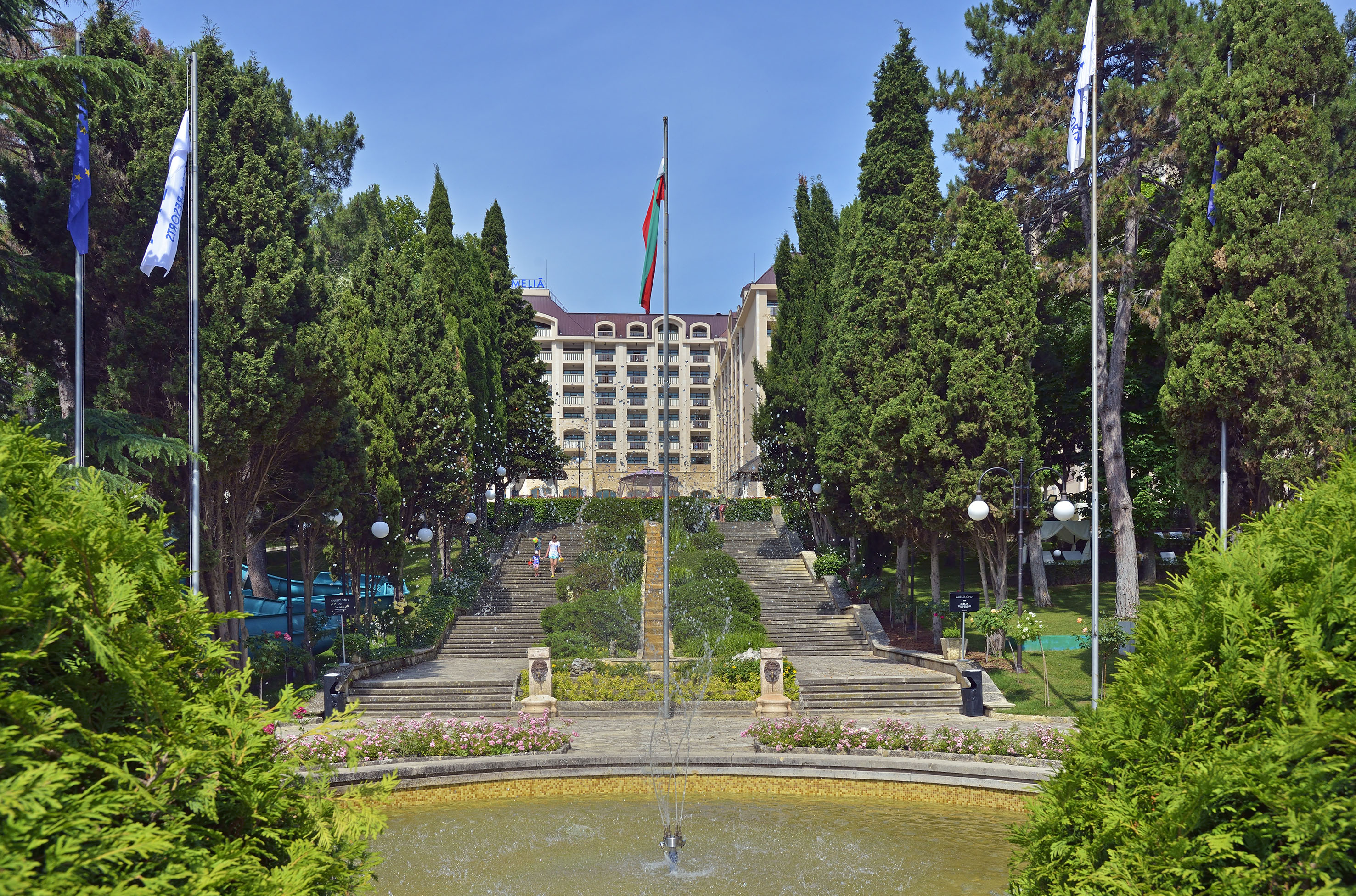 a fountain in a park with trees and a building in the background