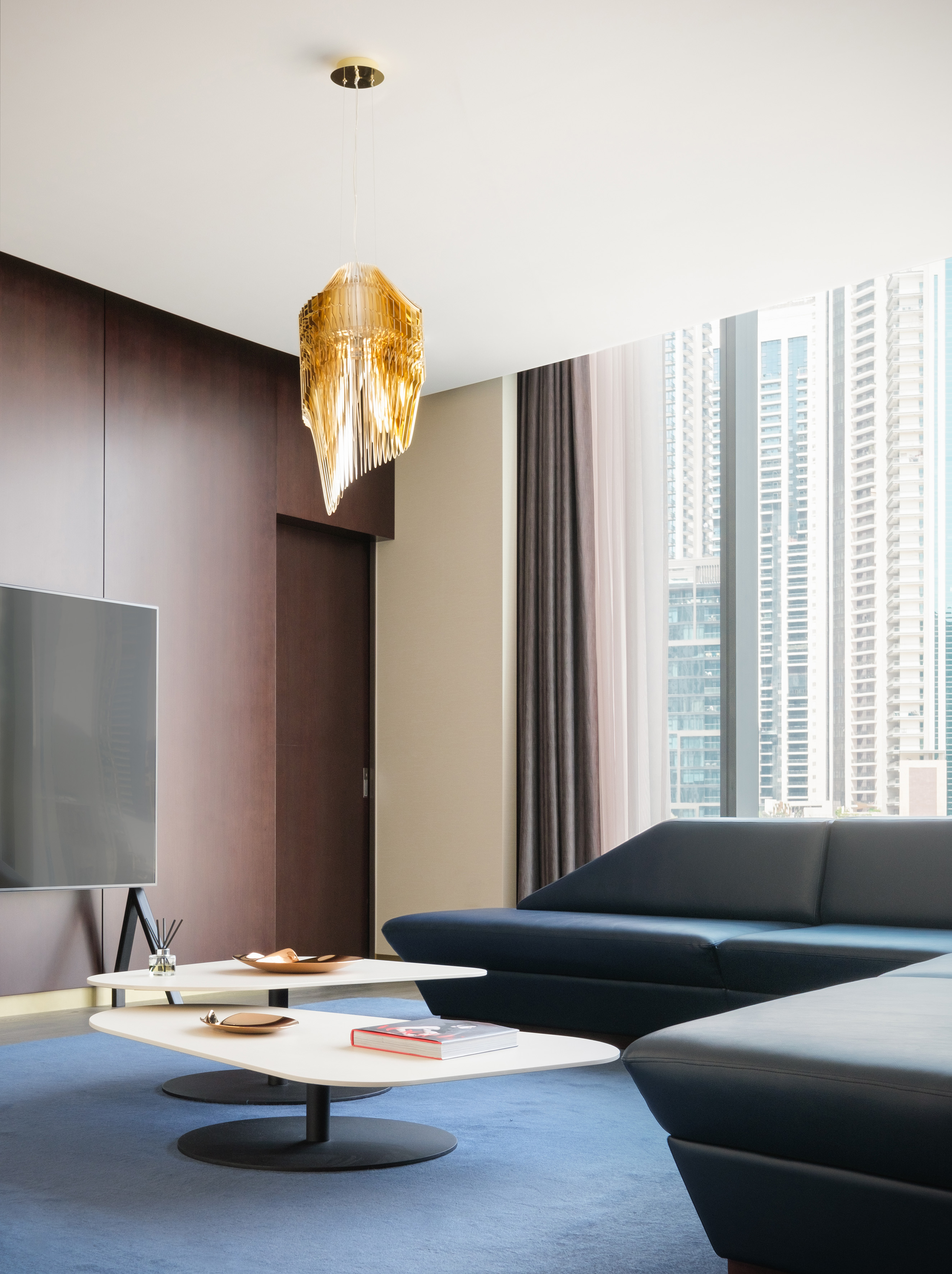 Luxury apartment living room with blue sofa, gold chandelier, skyscrapers.