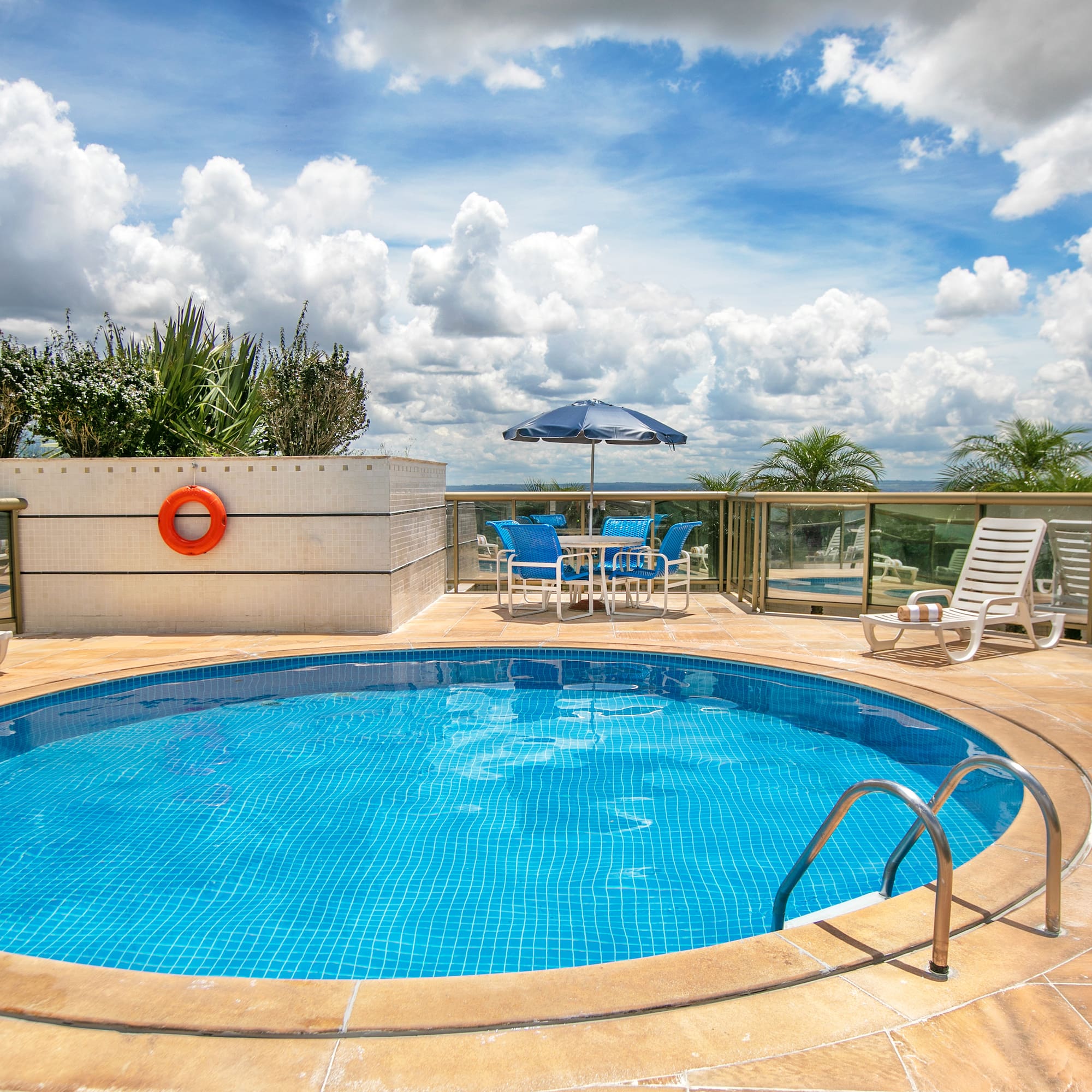 Sunny hotel rooftop pool with blue tiled water, chairs, and umbrella.
