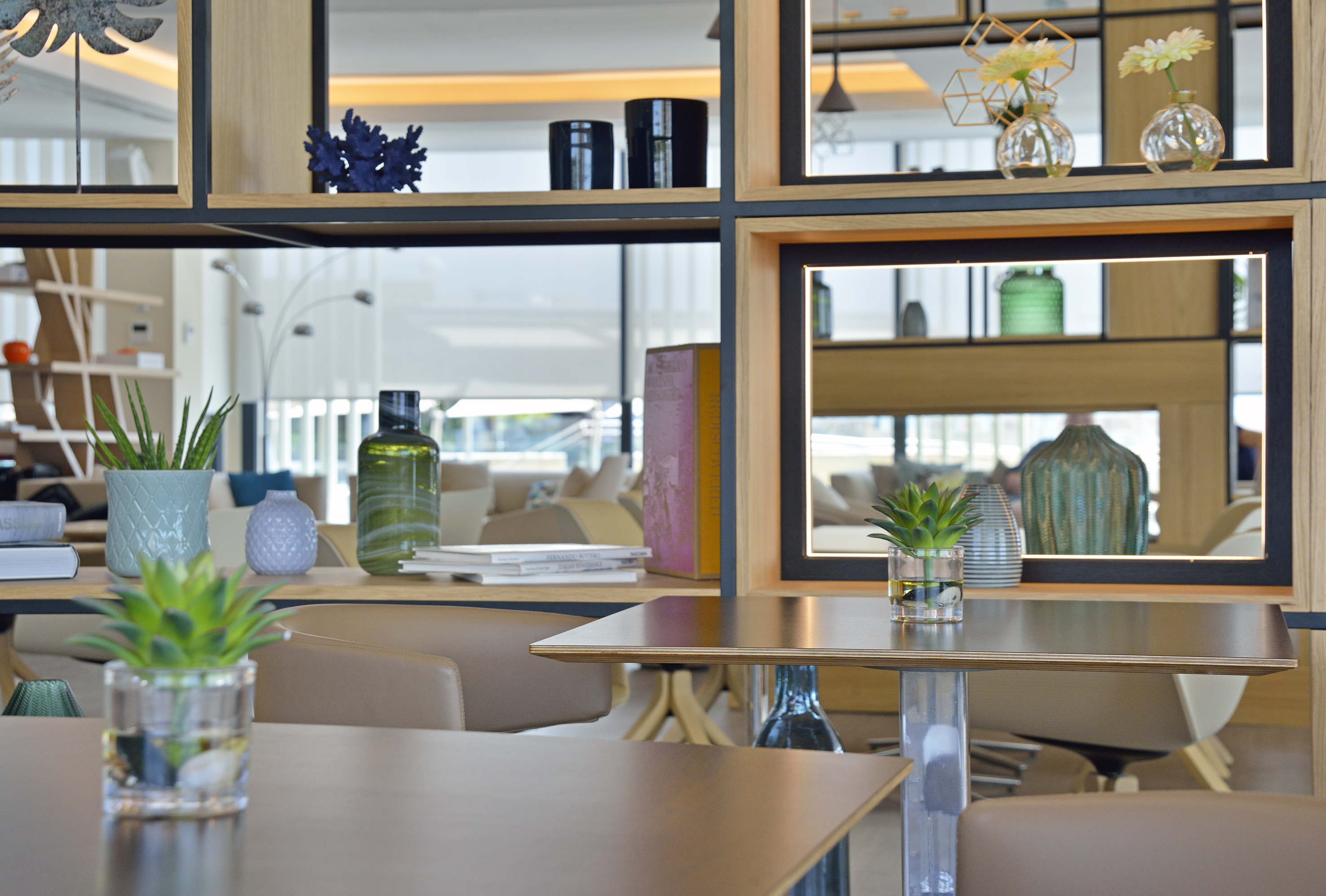 Modern room divider with wooden shelves, decorative plants, and cafe tables.