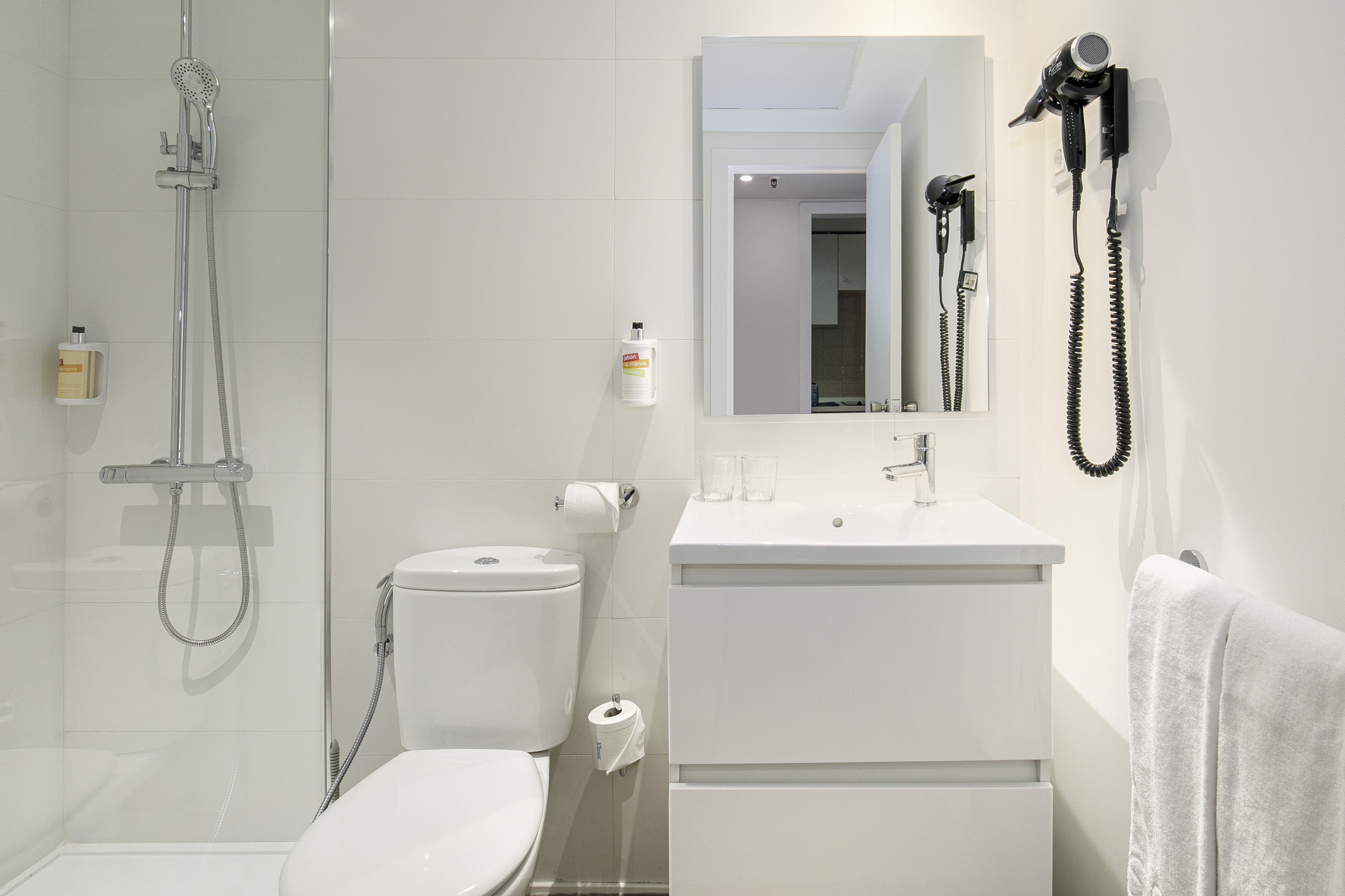Modern white bathroom with shower, toilet, vanity, mirror, and hairdryer.