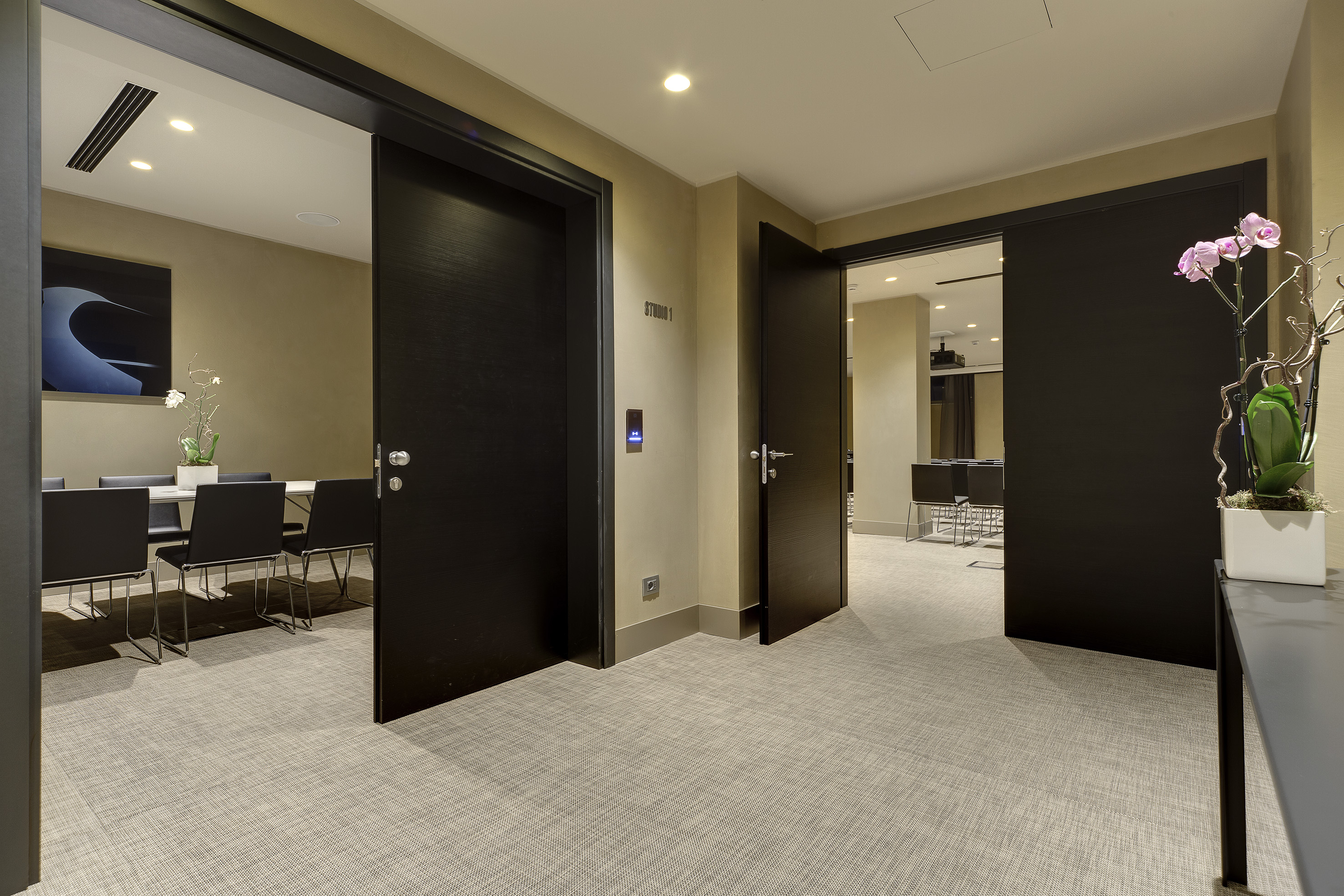 Modern corridor to hotel meeting rooms/studios, dark doors open, carpeted.