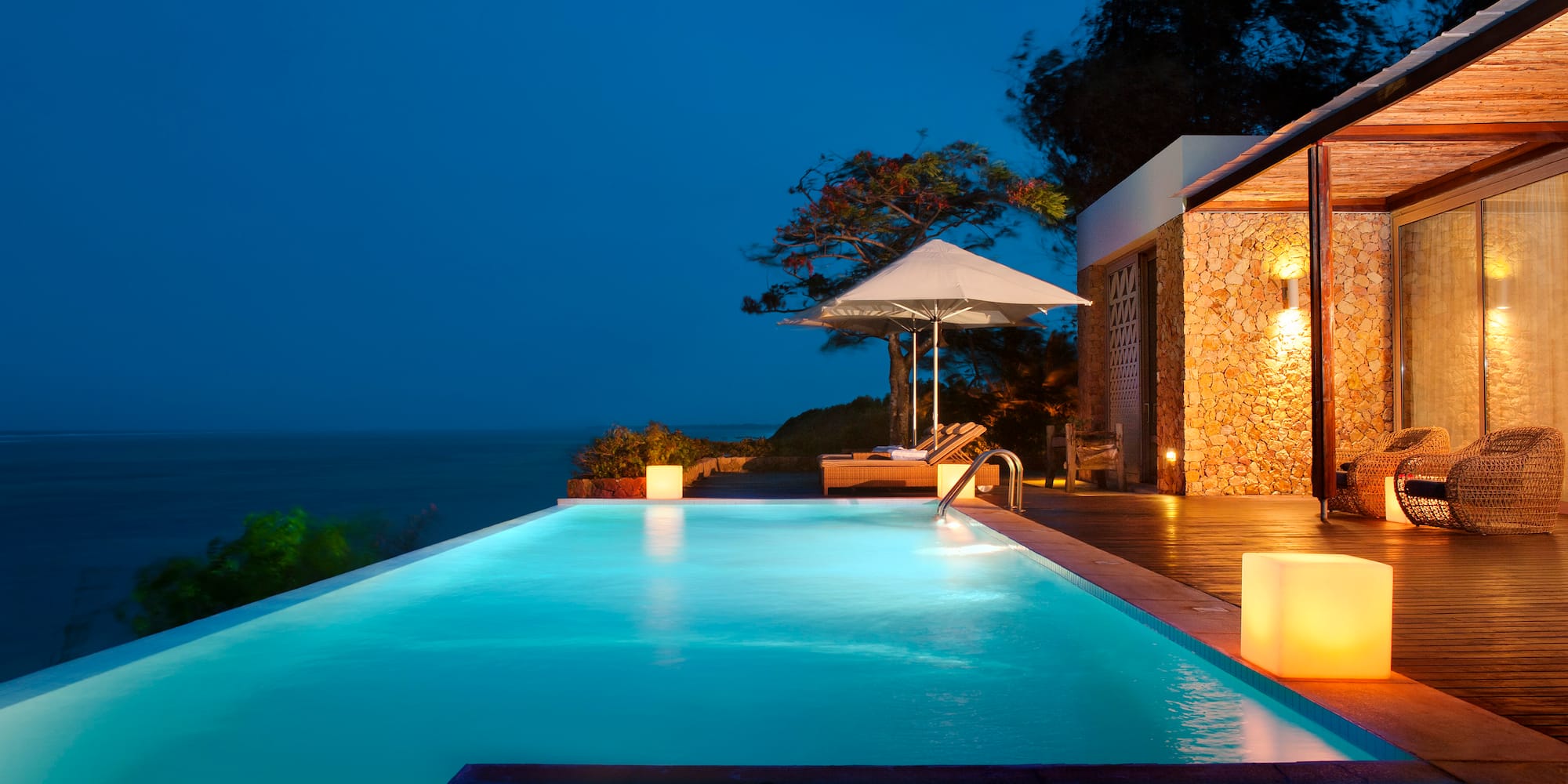 a pool with a deck and umbrella and a building with trees and a blue sky