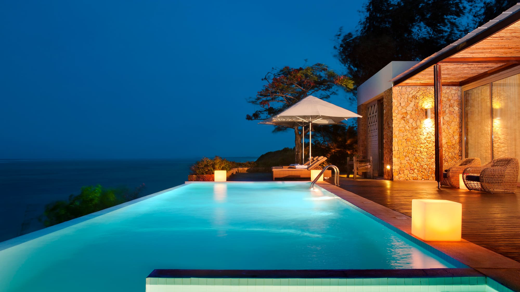 a pool with a deck and umbrella and a building with trees and a blue sky