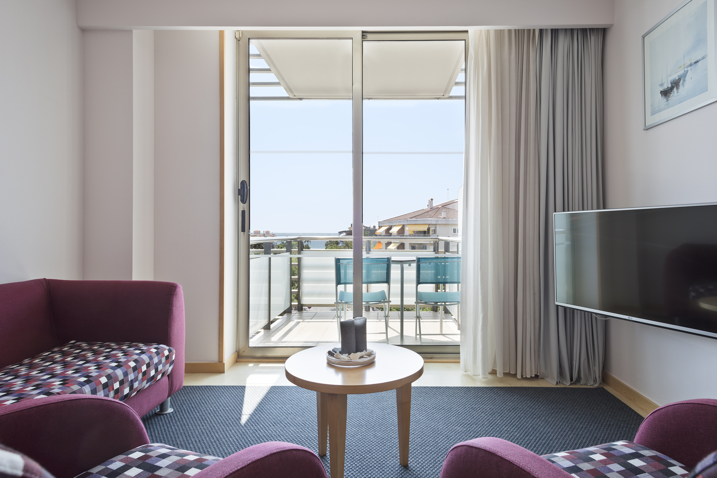 Modern hotel suite living room with balcony, ocean view, purple seating.