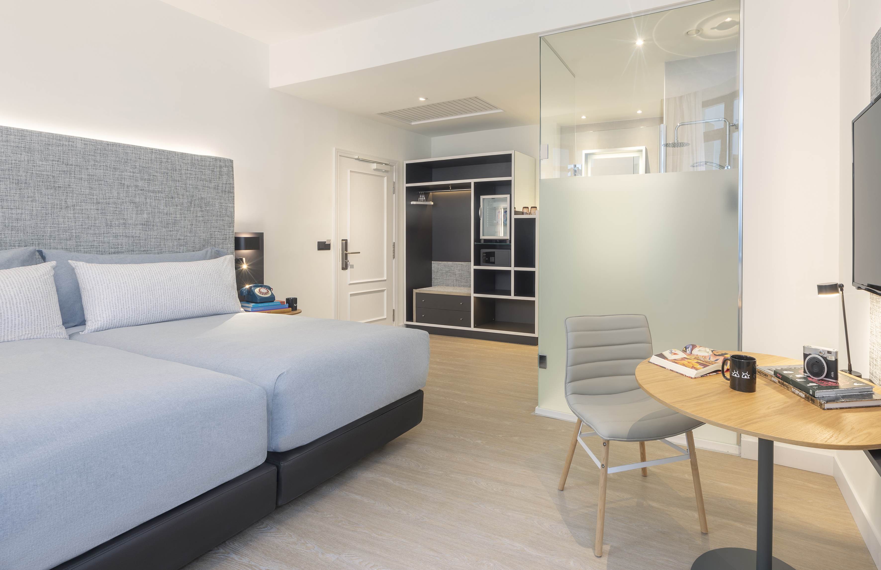 Contemporary hotel room featuring twin beds, open closet, and work desk.