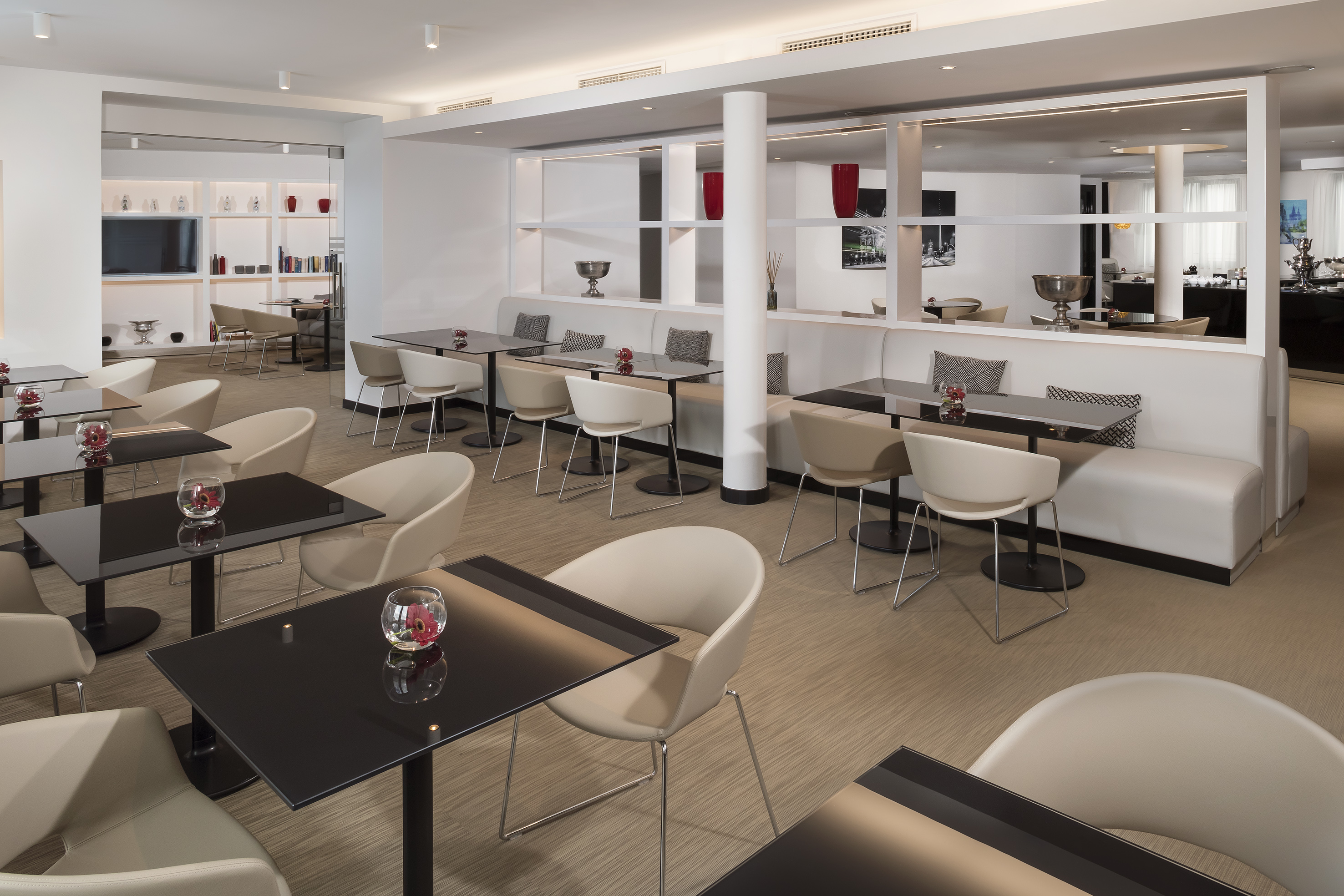 Modern hotel dining lounge with black tables and light beige chairs.