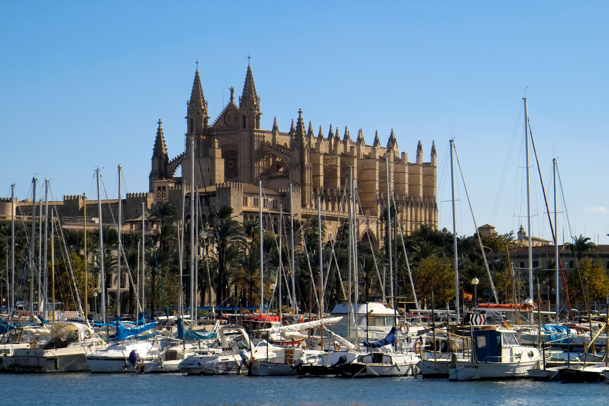 a castle with many boats in the water with Palma Cathedral in the background