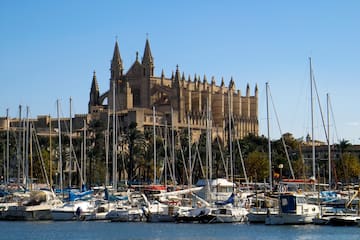 a castle with many boats in the water with Palma Cathedral in the background