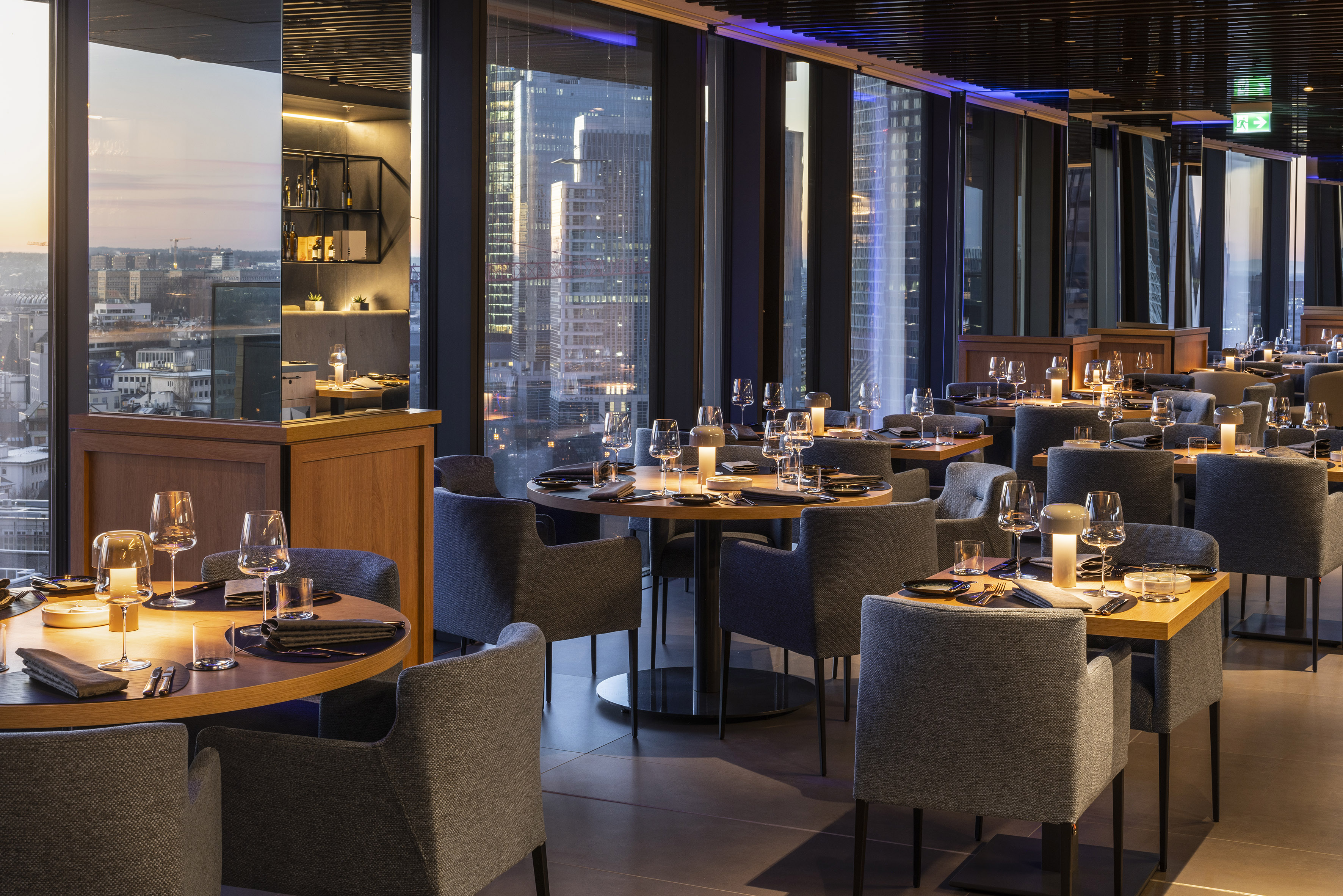 Panoramic restaurant with city skyline view, modern tables, and ambient lighting.