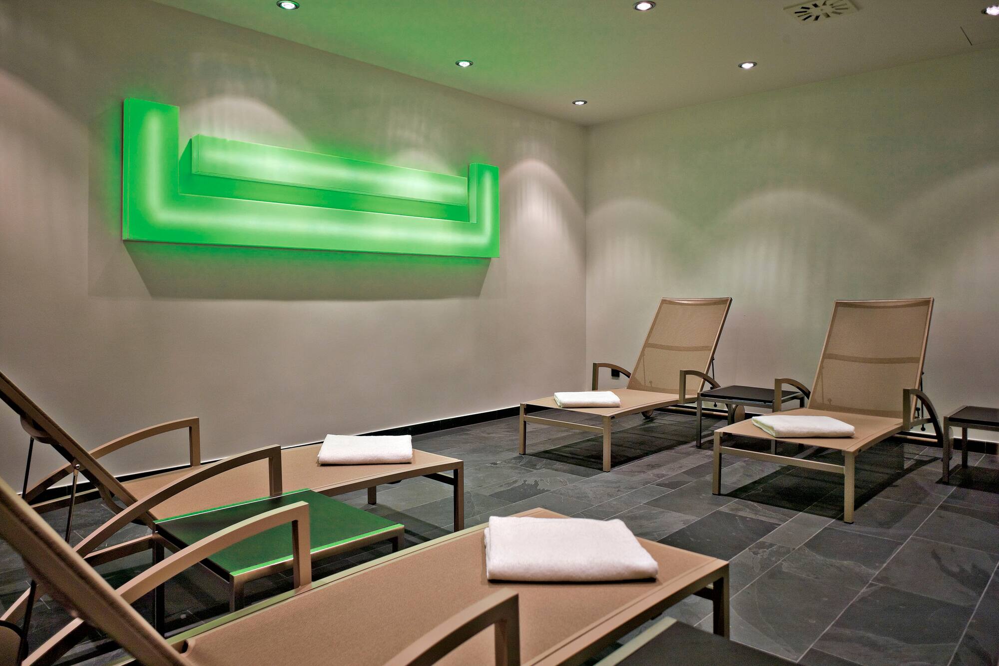 Modern spa relaxation room with daybeds, ambient green light, and dark floor.