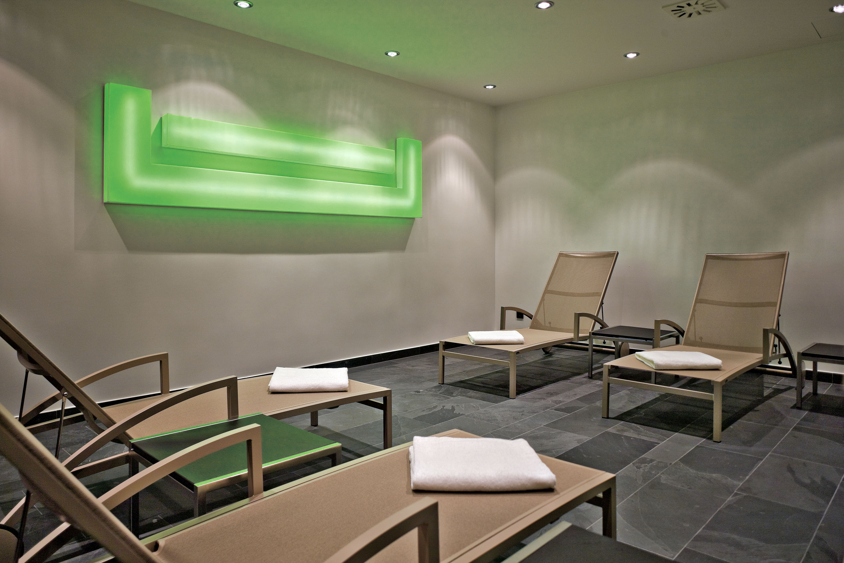 Modern spa relaxation room with daybeds, ambient green light, and dark floor.