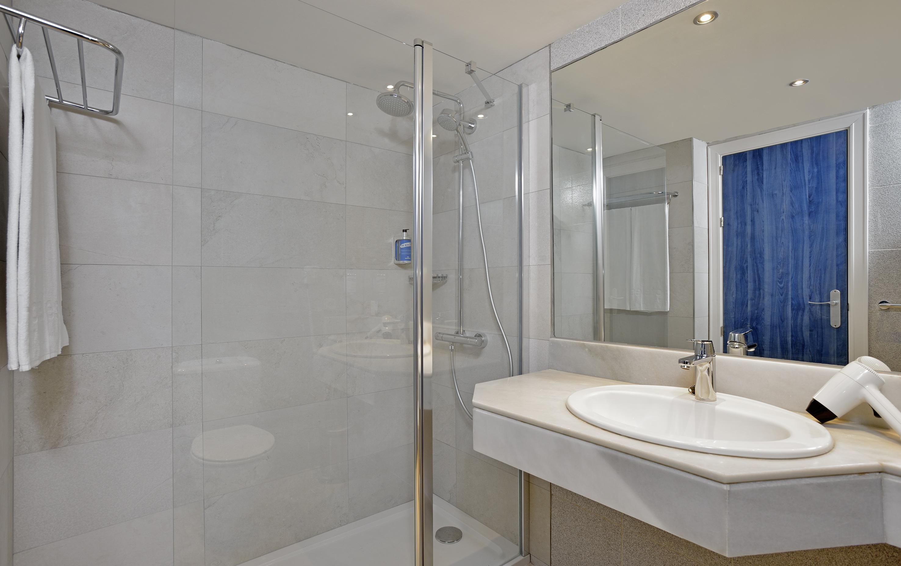 Hotel bathroom with tiled walls, glass shower, toilet, vanity sink, mirror.